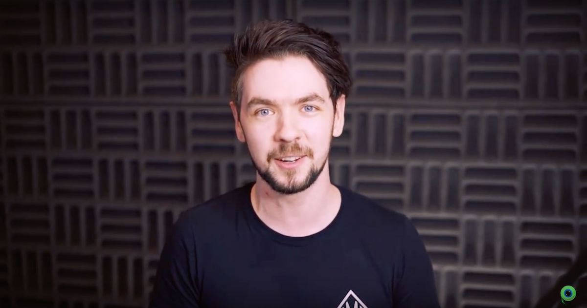 Jacksepticeye 桌布 壁紙 — 一個藍眼睛、留鬍鬚的男人在深色幾何聲學牆前對著鏡頭微笑。