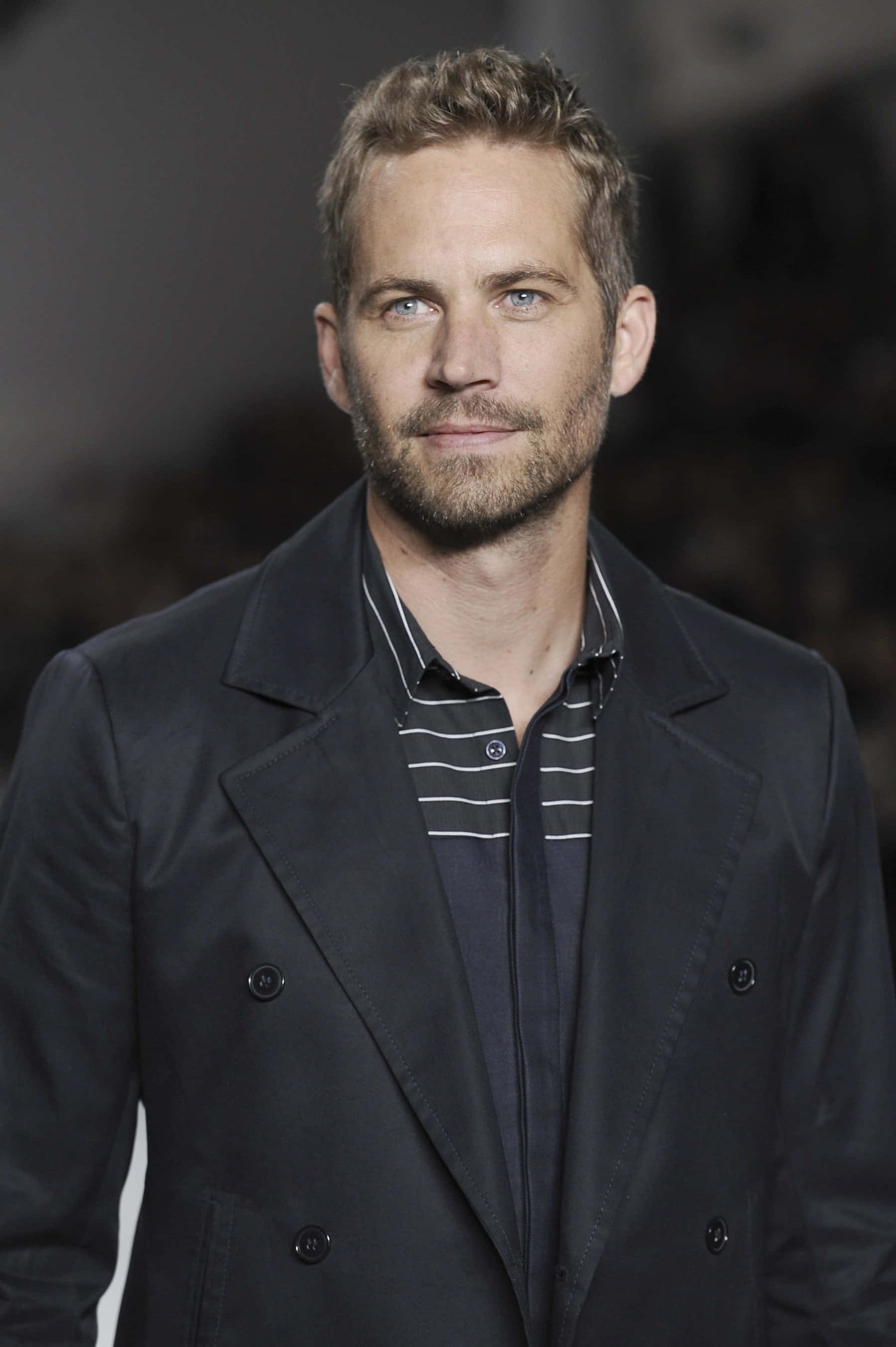 Paul Walker 桌布 壁紙 — 一個藍眼睛、鬍渣的男人，在模糊背景前，在條紋襯衫外面穿著一件深色外套。
