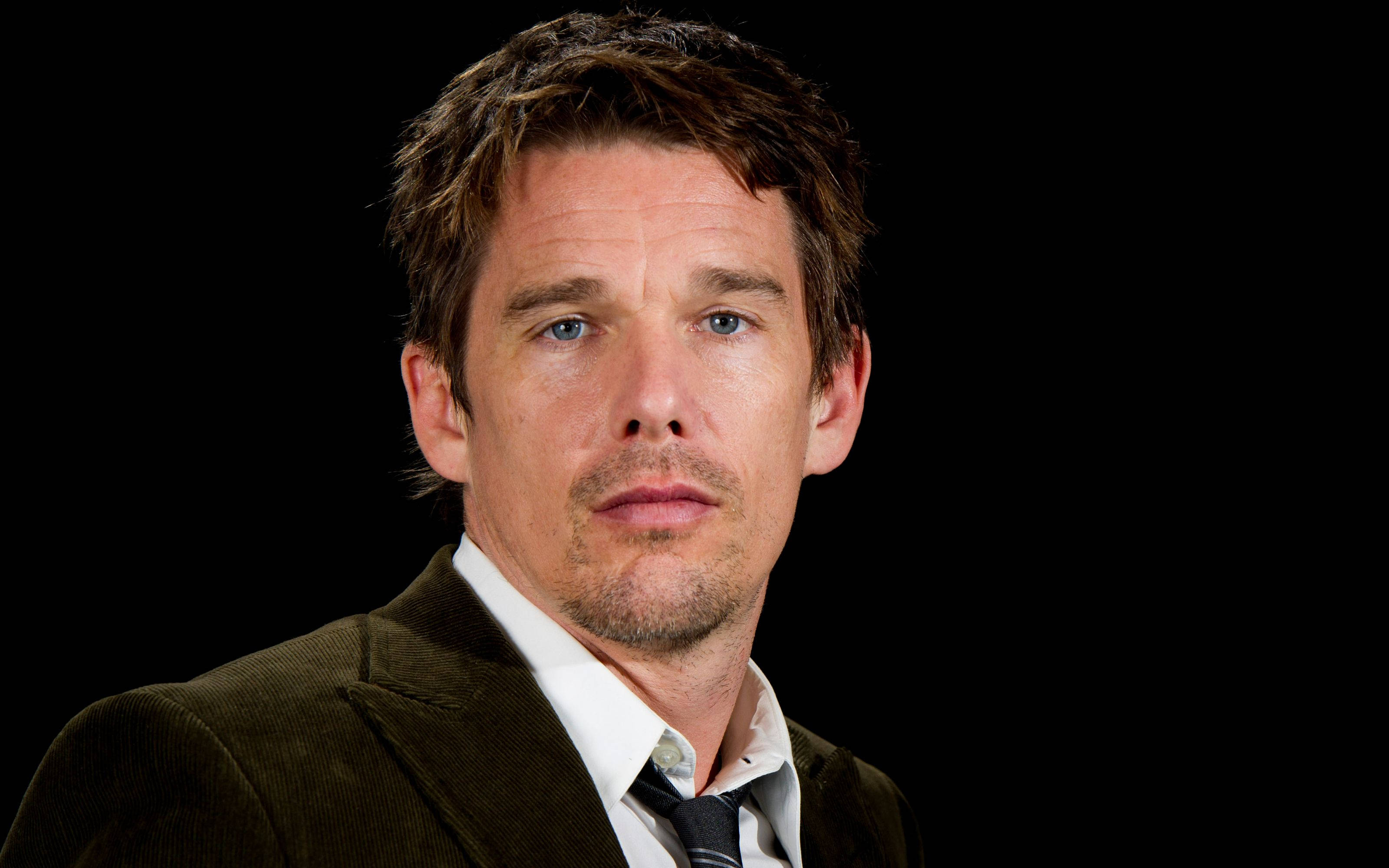 ethan hawke 桌布 壁紙 — 一個藍眼睛、鬍渣的男人，在黑色背景前穿著棕色燈芯絨外套，內搭白襯衫和領帶。
