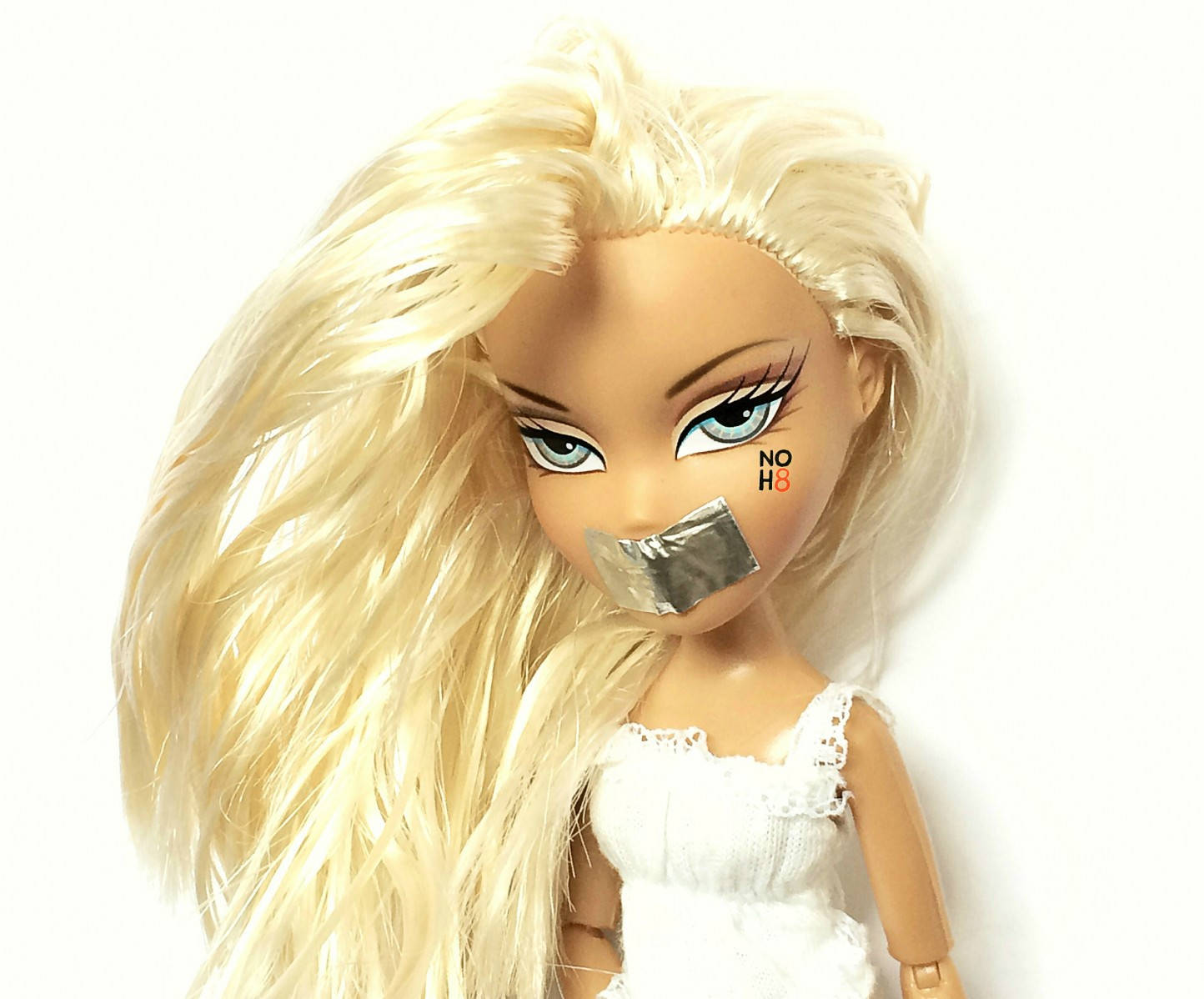 bratz 美學 桌布 壁紙 — 一個藍眼睛的金髮娃娃，嘴上貼著銀色膠帶，臉頰上寫著「NO H8」。