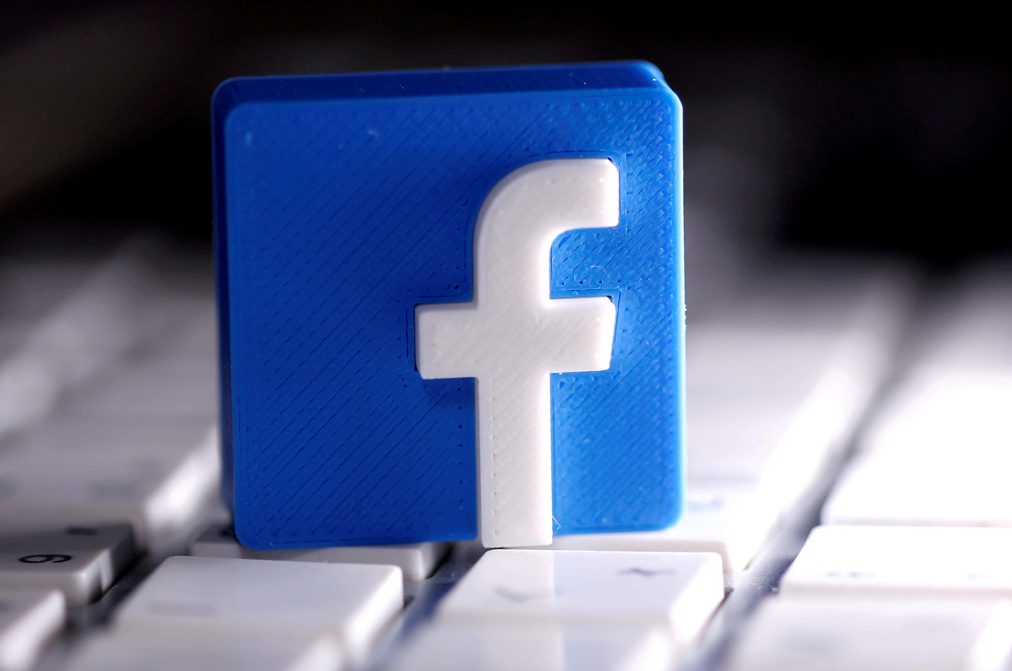 Facebook 桌布 壁紙 — 一個藍色3D列印的Facebook標誌立方體顯眼地放在一個白色電腦鍵盤上，景深較淺。