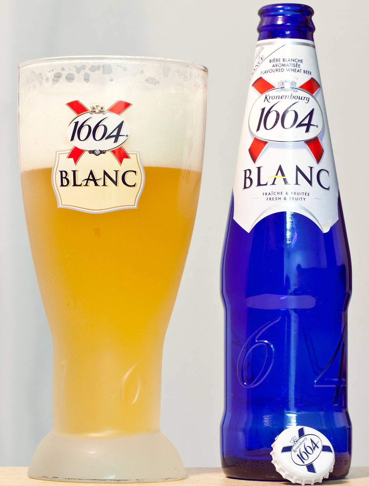 Fruits 桌布 壁紙 — 一個藍色Kronenbourg 1664 Blanc酒瓶和一個裝滿金色啤酒和白色泡沫的玻璃杯，背景單一。