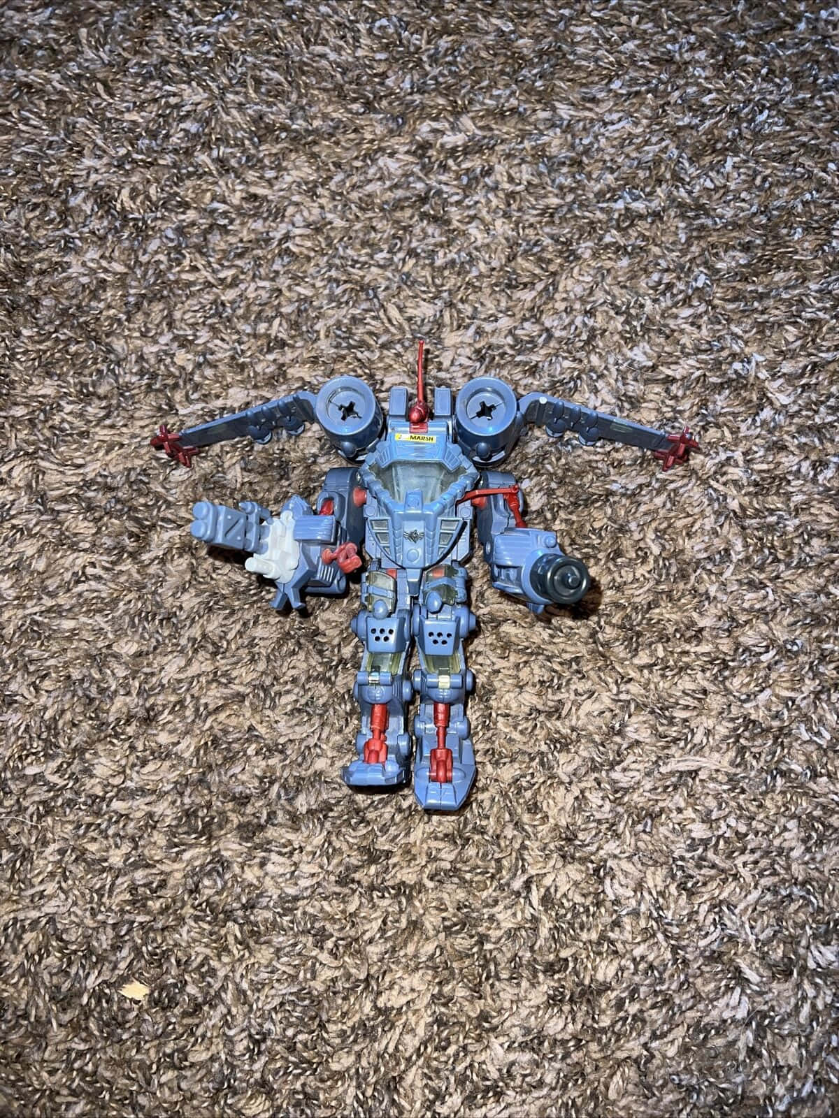 toys 桌布 壁紙 — 一個藍色和紅色的機器人玩具，有關節的四肢，躺在有紋理的棕色地毯上。