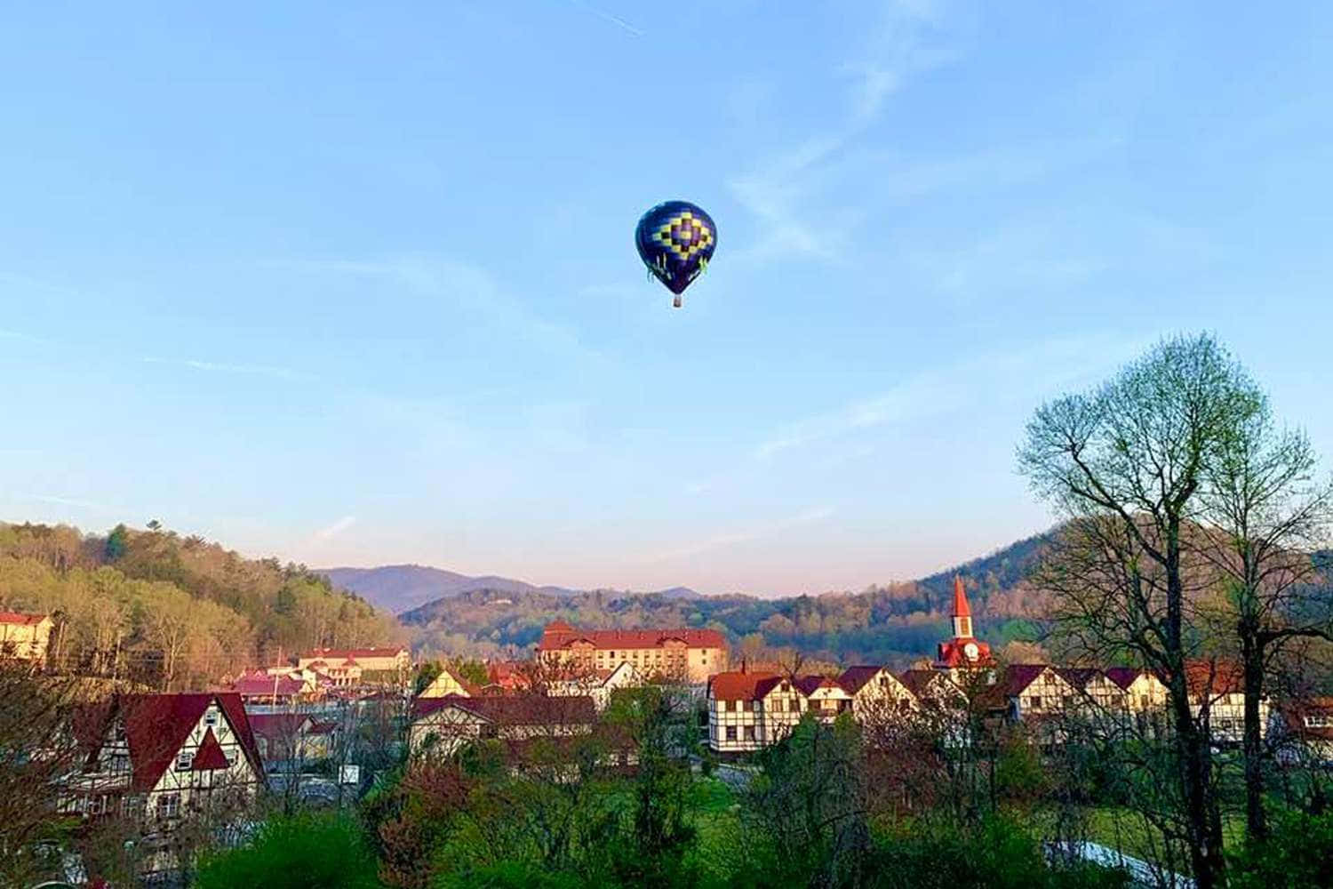 Balloon 桌布 壁紙 — 一個藍色圖案的熱氣球漂浮在一個坐落在綠色山丘中的古雅歐洲村莊上空，正值金色日落時分。