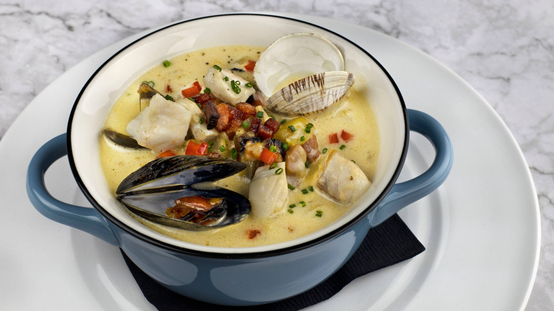 Chowder 桌布 壁紙 — 一個藍色手柄碗中的奶油海鮮濃湯，上面放有蛤蜊、淡菜、培根和細香蔥，置於大理石表面上。
