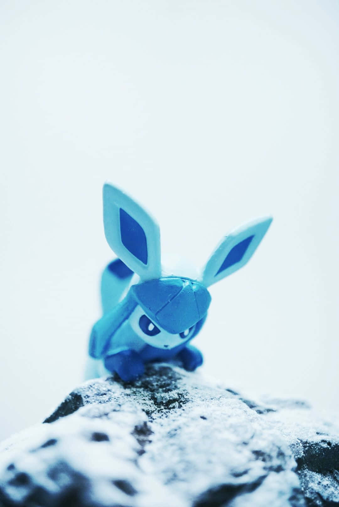 Pokemon Toys 桌布 壁紙 — 一個藍色毛絨伊布玩具棲息在灑滿白雪的石頭上，背景是明亮的白色。