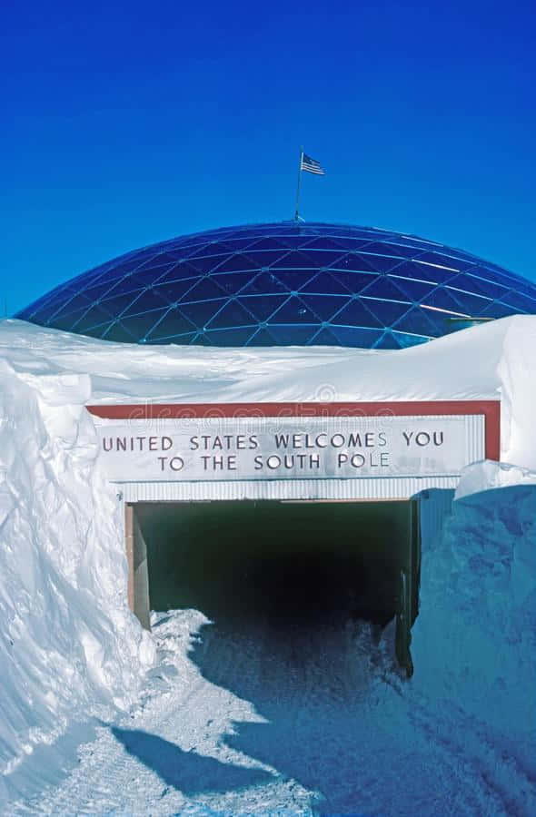 South Pole 桌布 壁紙 — 一個藍色測地線穹頂從純淨的雪地中冒出，在清澈的藍天下，有一個寫著「United States Welcomes You to the South Pole」的標誌。