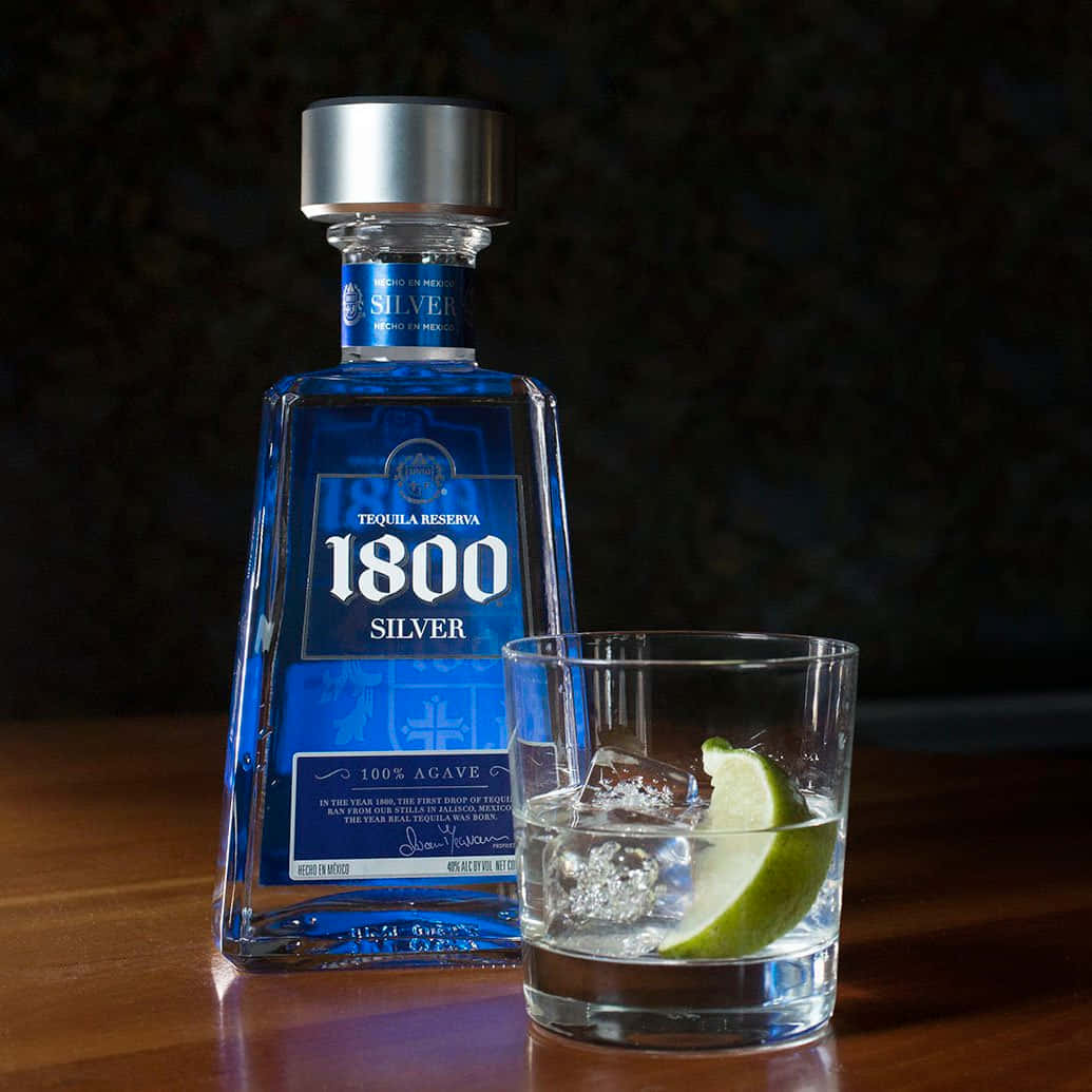 alcohol 桌布 壁紙 — 一個藍色的1800 Silver龍舌蘭酒瓶立在木質表面上的岩石杯（有冰塊和萊姆角）旁邊。