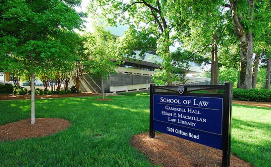 Lawyer 桌布 壁紙 — 一個藍色的法學院標誌矗立在陽光明媚的草地上，周圍環繞著茂密的綠樹，背景是一座現代建築。
