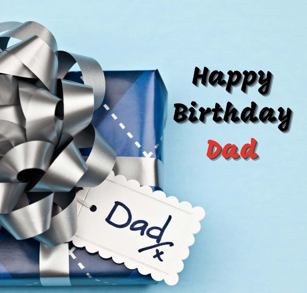 daddy 桌布 壁紙 — 一個藍色禮物盒，帶有銀色蝴蝶結和標有「Dad」的標籤，放在淺藍色背景上，並有「Happy Birthday Dad」文字。