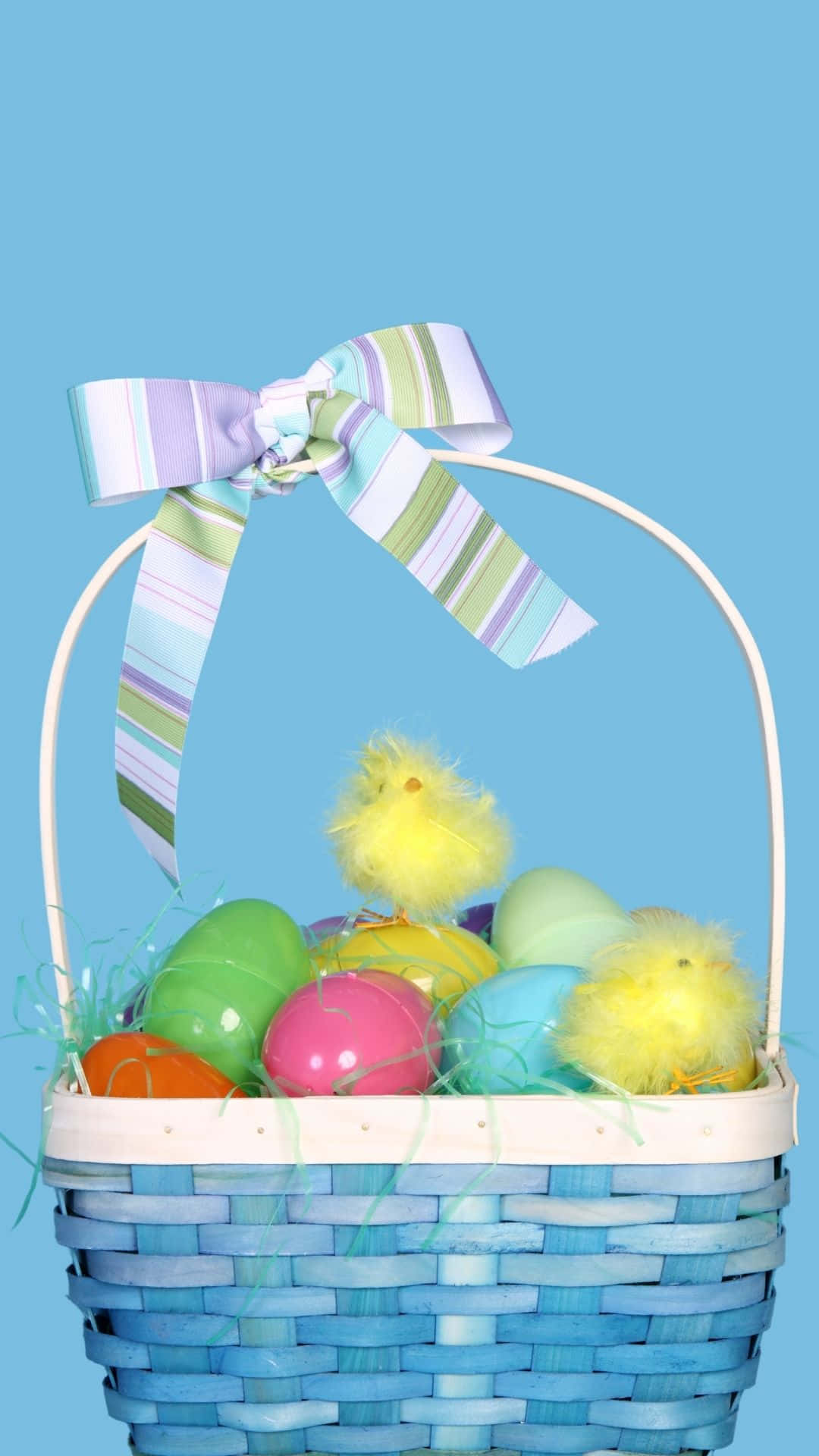 Easter Basket 桌布 壁紙 — 一個藍色編織復活節籃子，裝滿彩色雞蛋和毛茸茸的小雞，背景是純淺藍色。