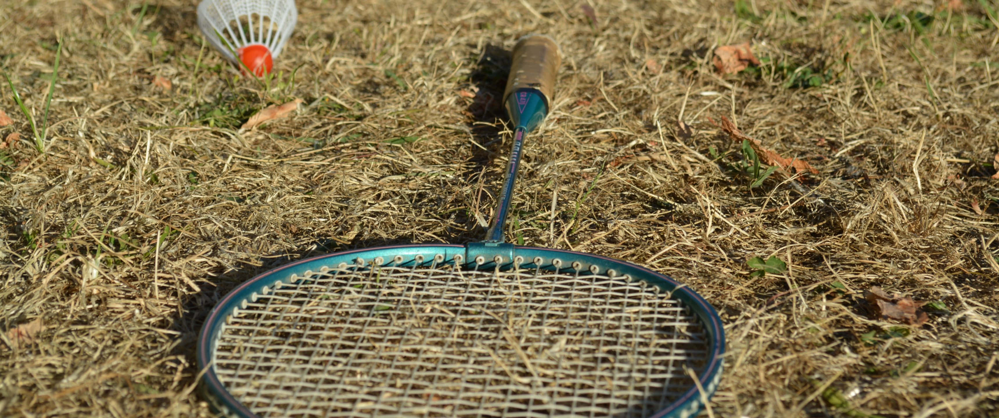 3440x1440p Badminton 桌布 壁紙 — 一個藍色羽毛球拍和羽毛球在明亮陽光下放在乾草上。