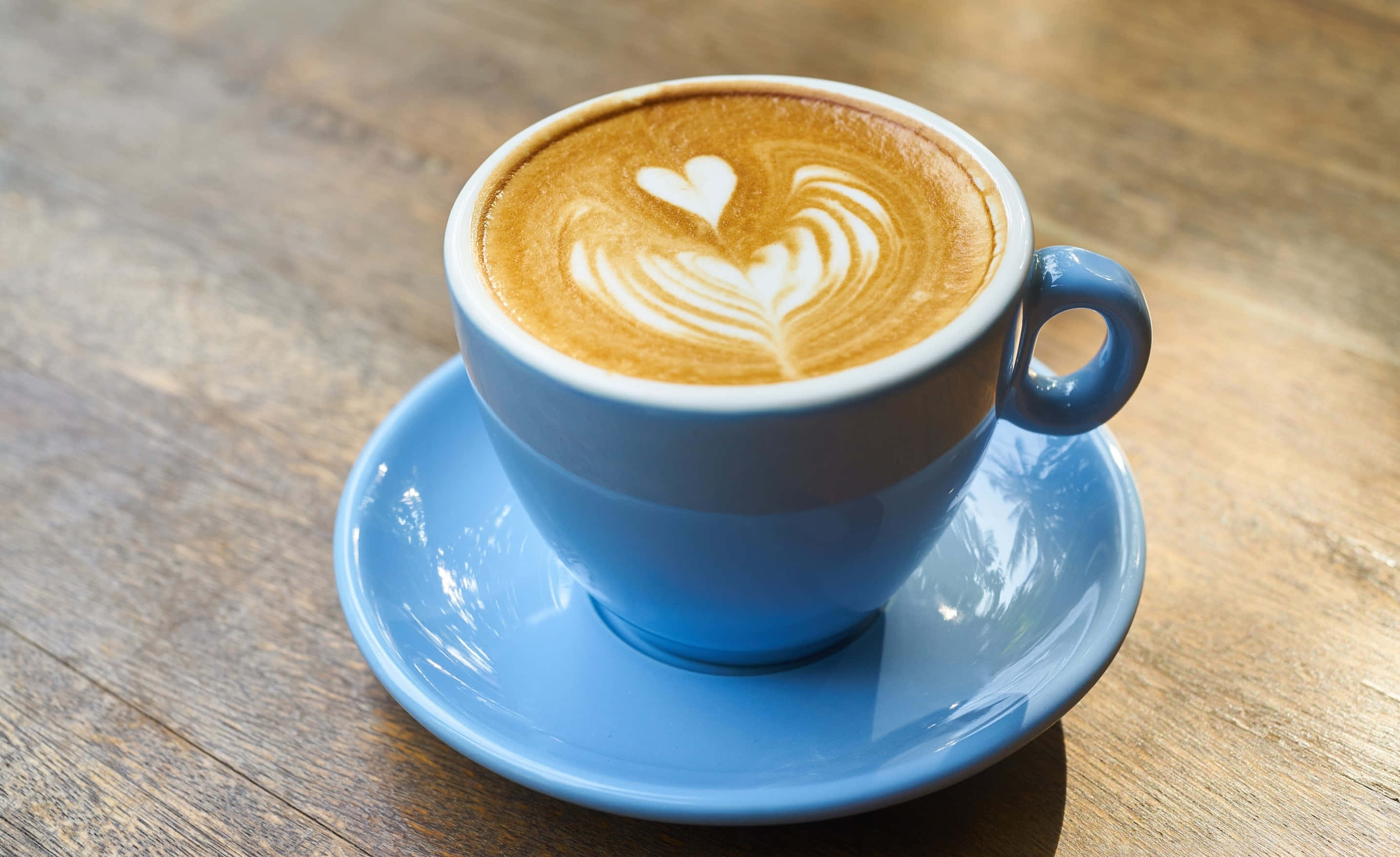 Coffee Aesthetic 桌布 壁紙 — 一個藍色陶瓷杯盛載著心形拉花藝術咖啡，放在相配的碟子上，置於鄉村風木桌上。
