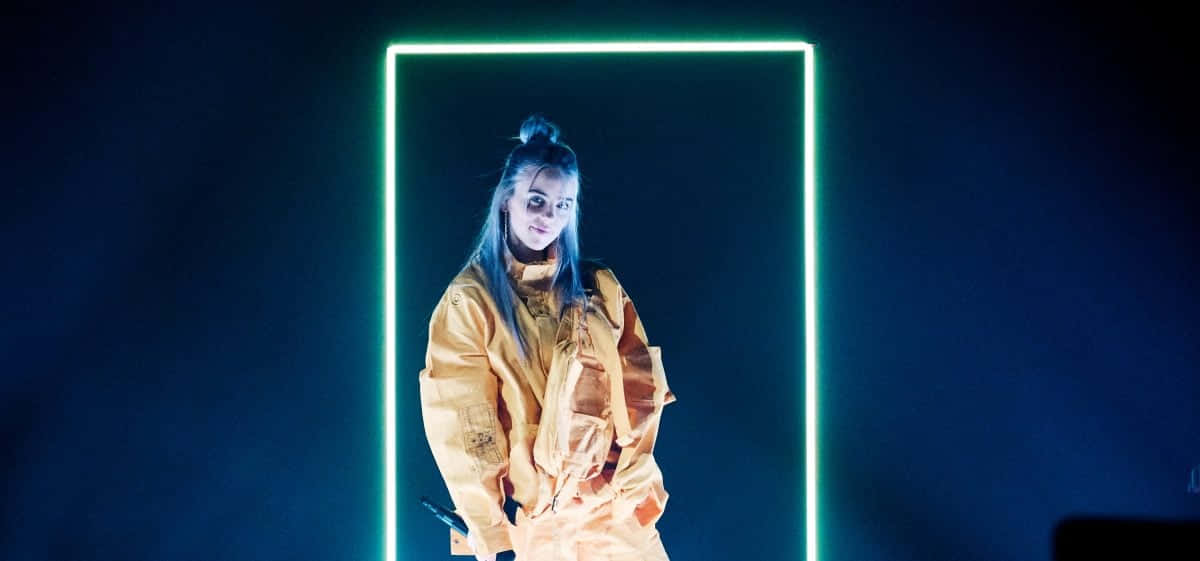 Billie Eilish Laptop 桌布 壁紙 — 一個藍色頭髮、穿著黃色外套的人，在深藍色背景下被發光的霓虹燈矩形框住。