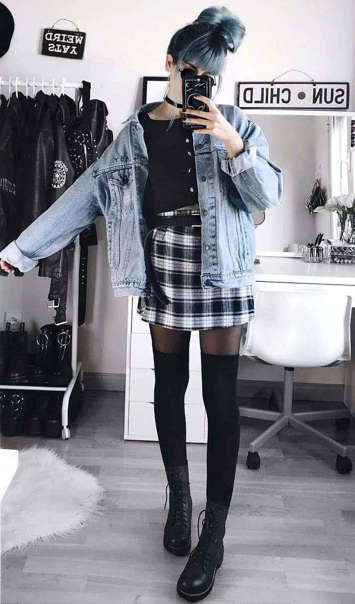 emo 美學 桌布 壁紙 — 一個藍色頭髮的人，在簡約的房間裡，穿著牛仔外套、格紋裙和黑色靴子，對著鏡子自拍。