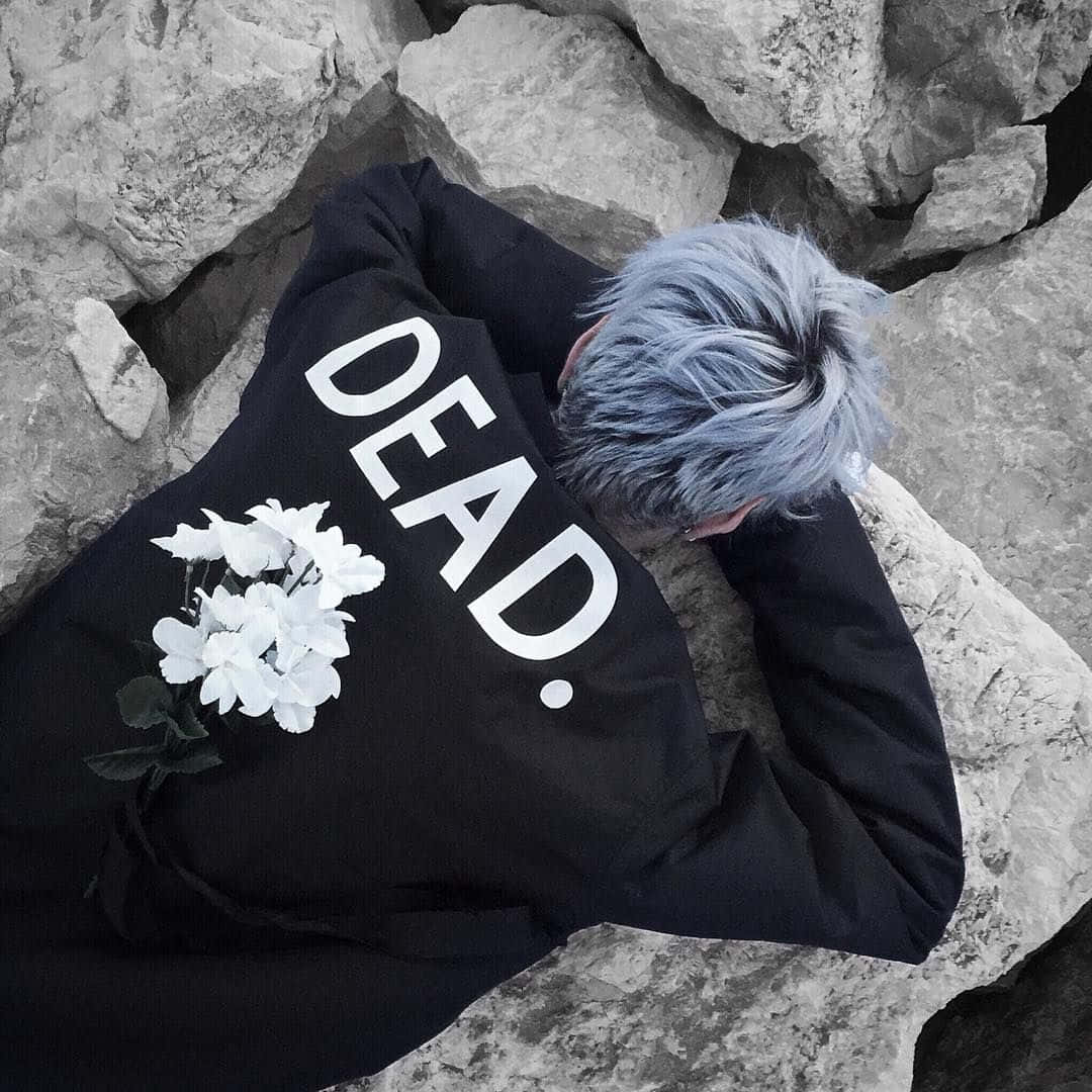 桌布 壁紙 — 一個藍色頭髮的人躺在灰色岩石上，穿著一件黑色連帽衫，上面印有白色的「DEAD.」，背上放著白色花朵。