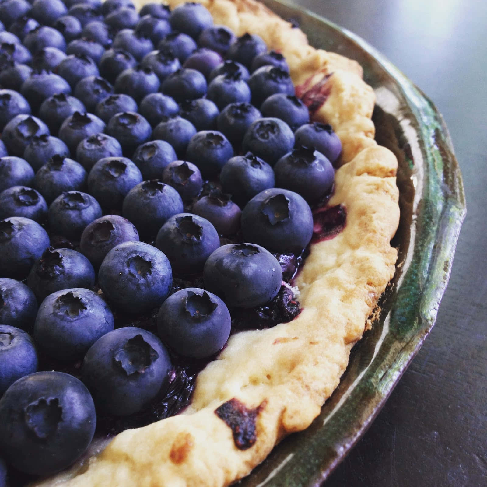 Blueberries Tart 桌布 壁紙 — 一個藍莓派的特寫，帶有閃亮的莓果和金黃色的派皮，放在一個鄉村風格的陶瓷盤上。