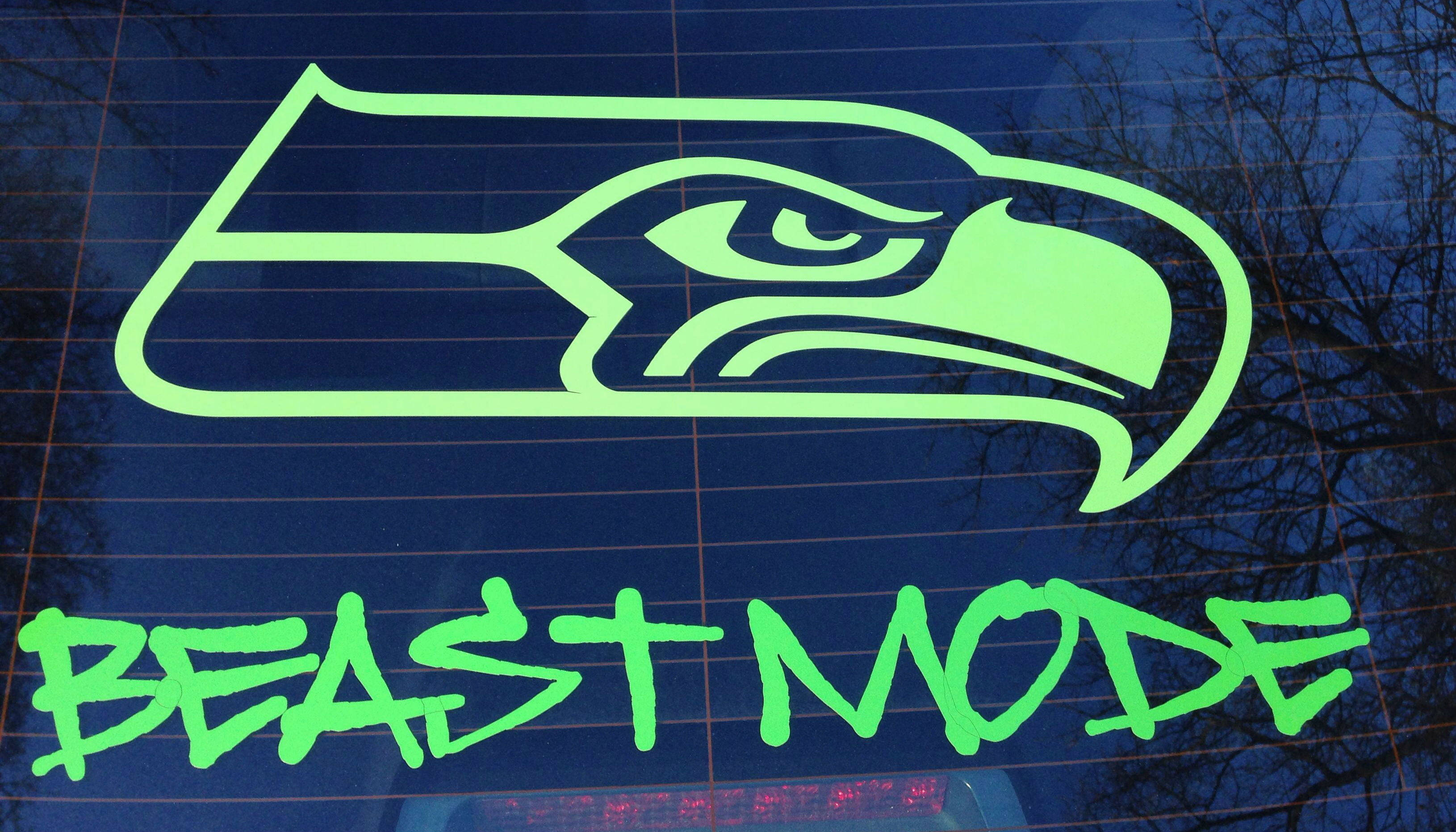 Seattle Seahawks 桌布 壁紙 — 一個螢光綠色的西雅圖海鷹隊標誌和「BEAST MODE」文字貼紙貼在汽車窗戶上，後面可見光禿的樹枝。