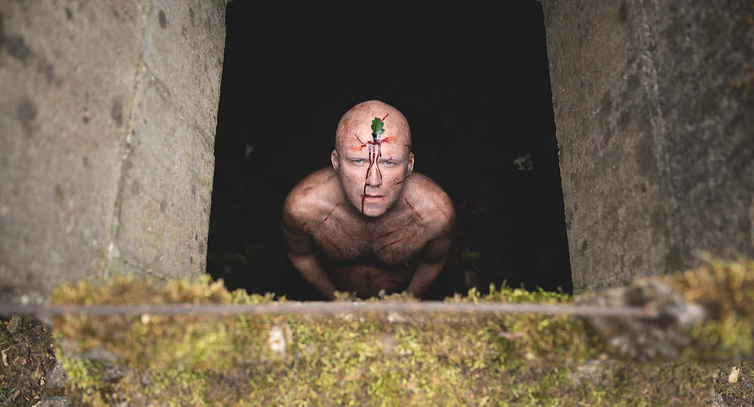 恐怖動圖 桌布 壁紙 — 一個血淋淋的男人，額頭上長出一棵綠色嫩芽，從長滿青苔的混凝土隧道中探出頭來。