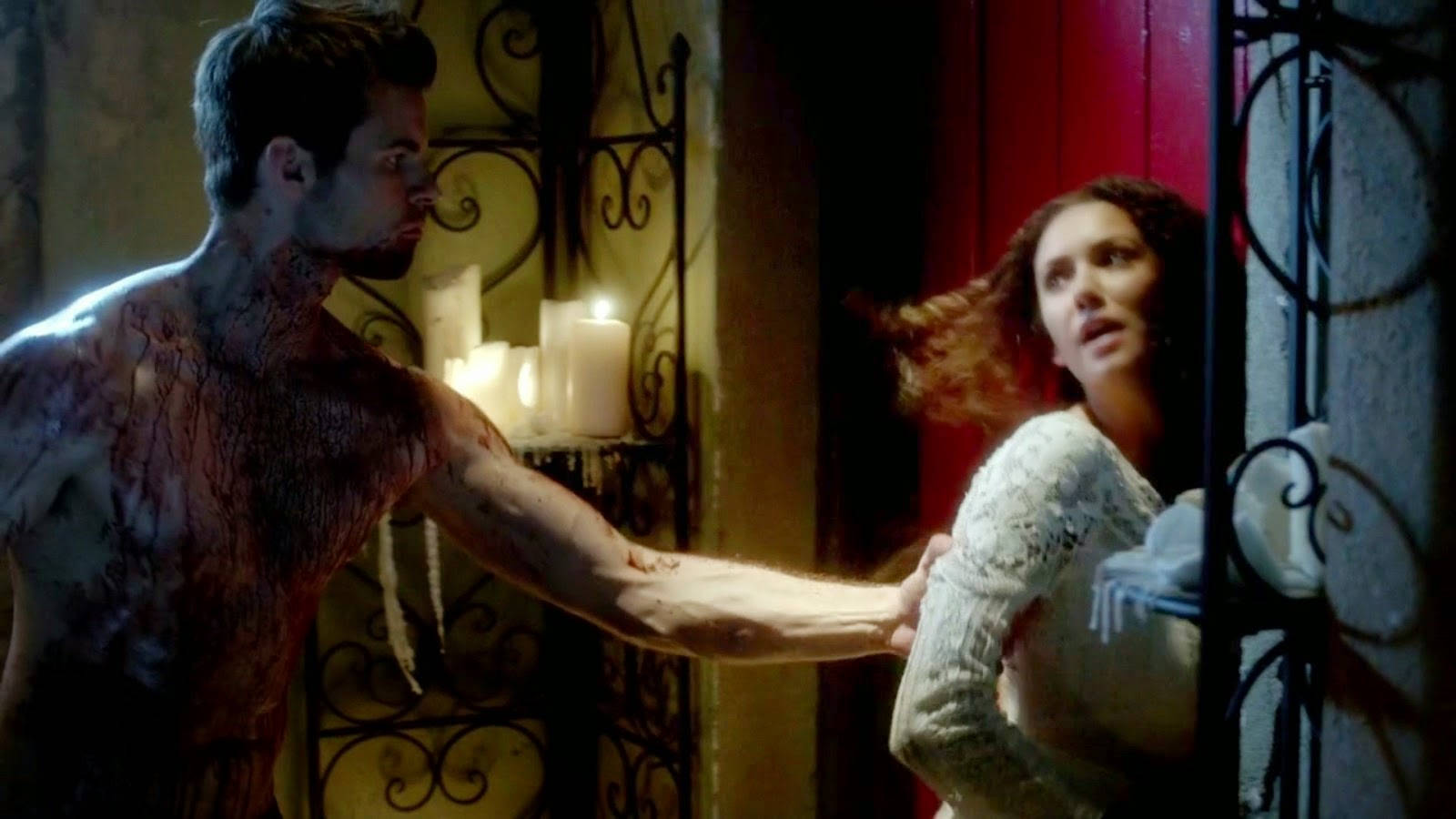 elijah mikaelson 桌布 壁紙 — 一個血淋淋的男人向一個驚恐的女人伸出手，身處燭光映照、帶有華麗鐵藝的哥德式房間。