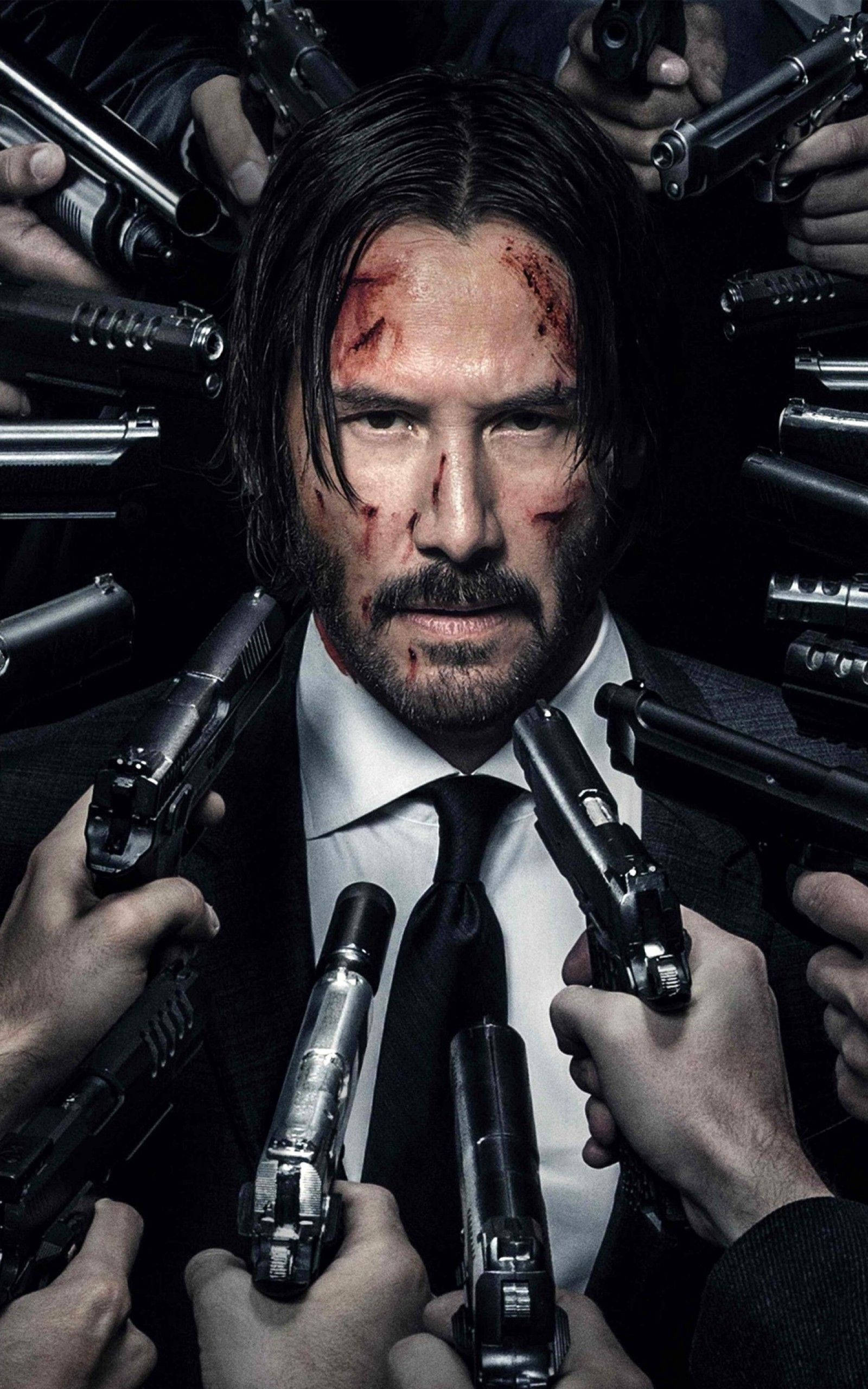 Keanu 桌布 壁紙 — 一個血跡斑斑、身穿西裝的男人在黑暗緊張的場景中，被多隻持槍的手包圍，他眼神銳利地凝視著。