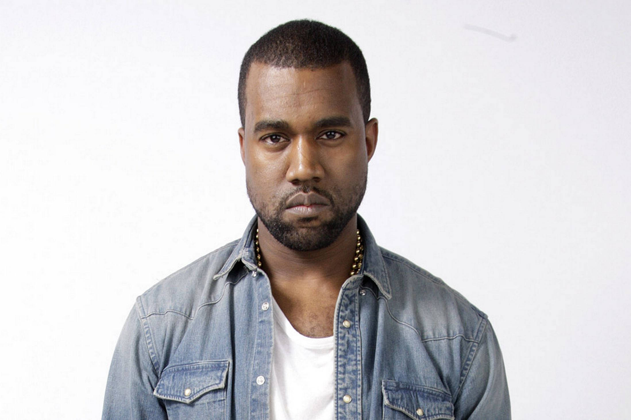 Kanye 桌布 壁紙 — 一個表情嚴肅的男人，身穿牛仔襯衫內搭白色T恤，背景為純白色。