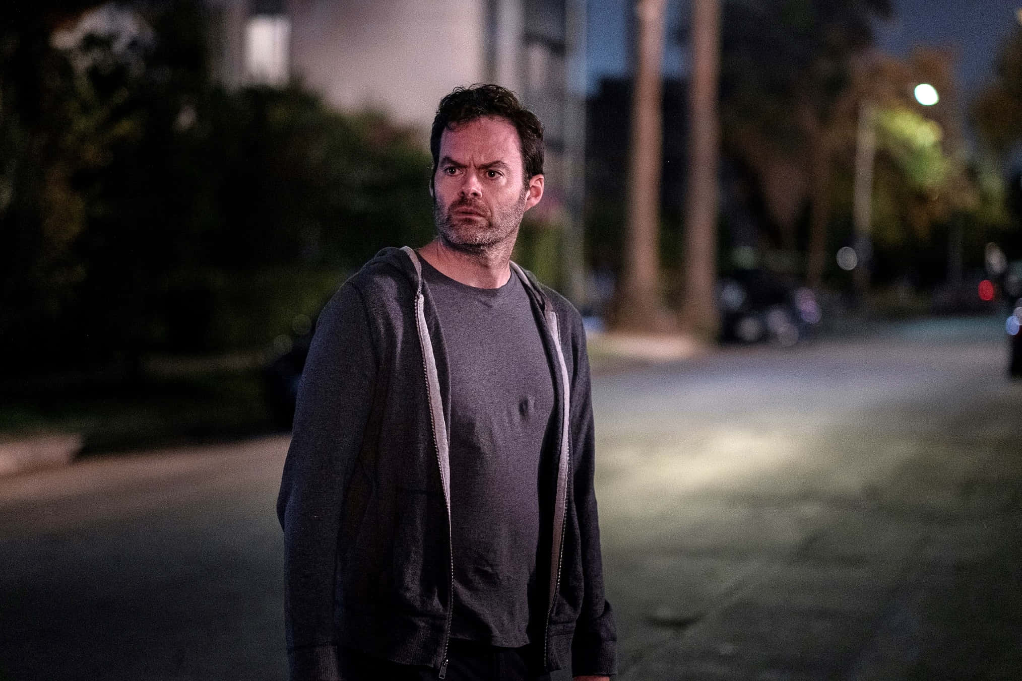 bill hader 桌布 壁紙 — 一個表情嚴肅的男人獨自站在夜晚昏暗的街道上，路燈下。