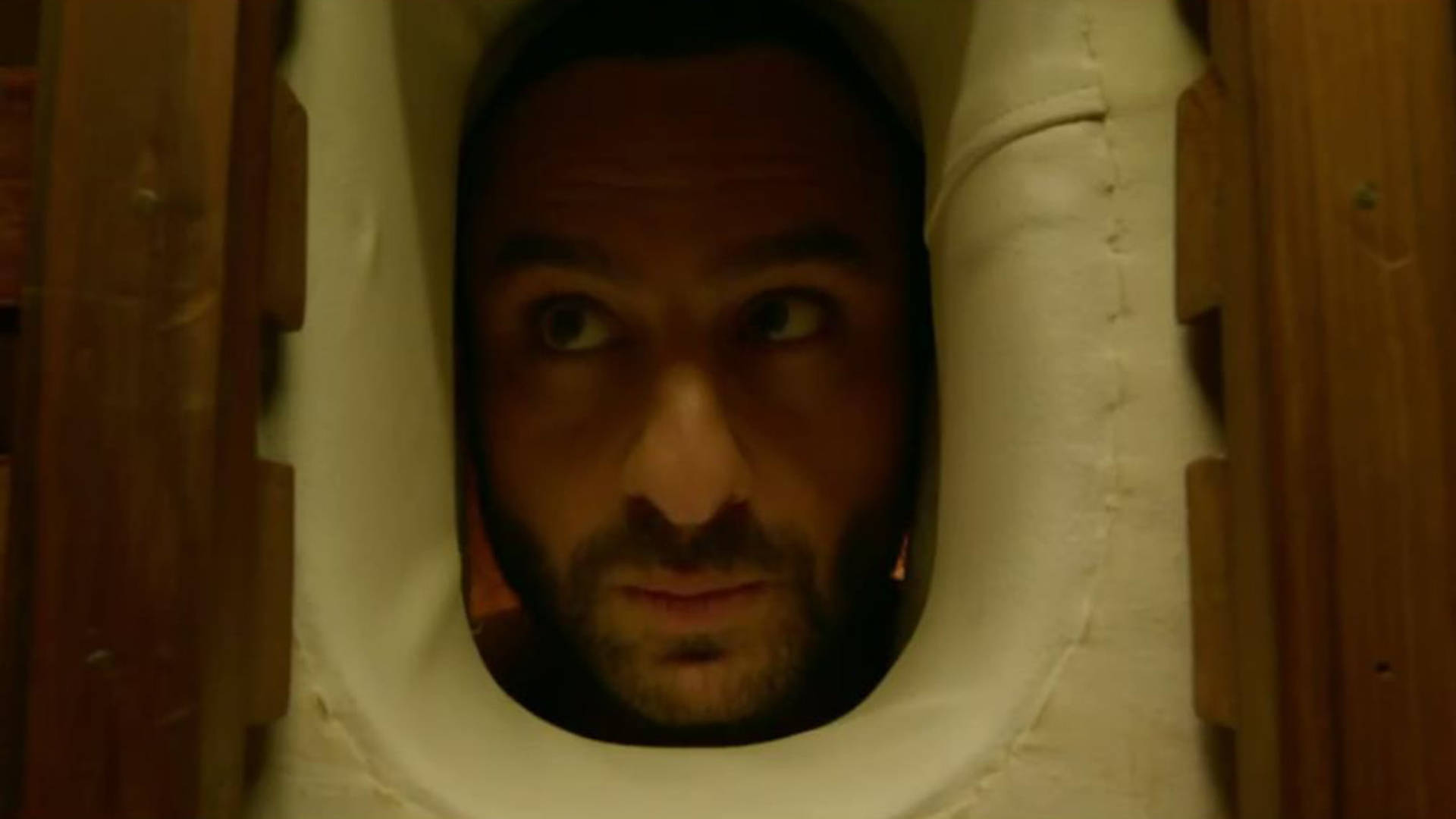 Saif Ali Khan 桌布 壁紙 — 一個表情驚恐的男人透過白色軟墊木結構上的一個小橢圓形開口窺視。