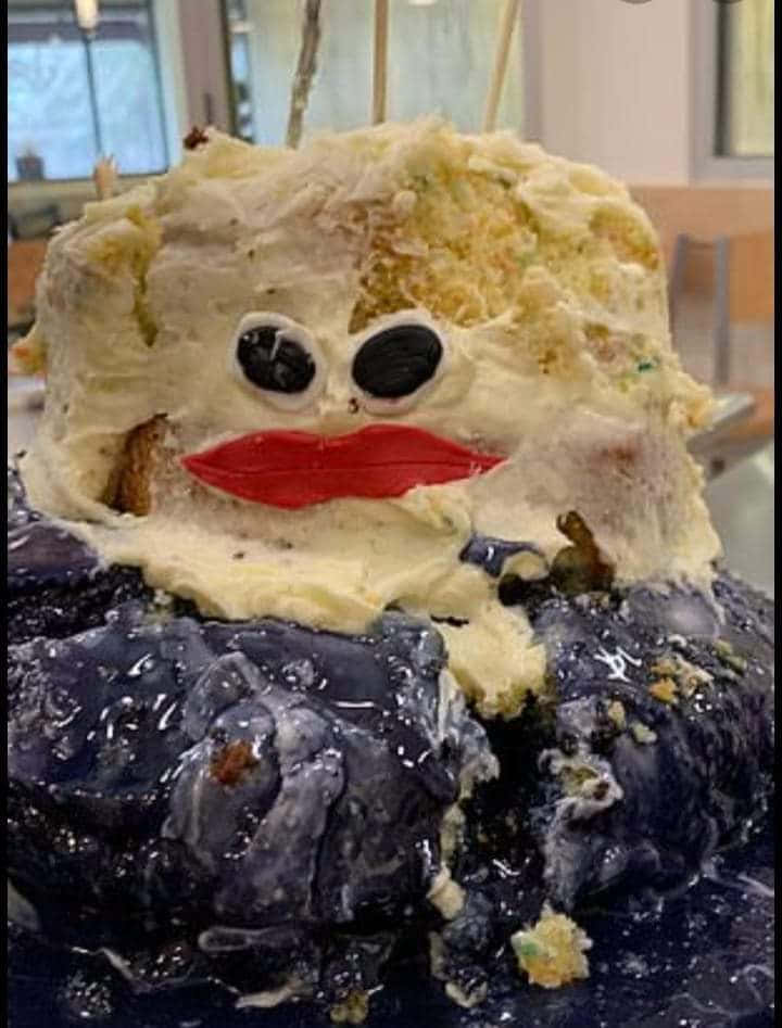 搞笑 桌布 壁紙 — 一個被吃了一半的蛋糕，有糖霜眼睛和紅色嘴唇，放在深紫色底座上，看起來像一個凌亂的卡通角色。