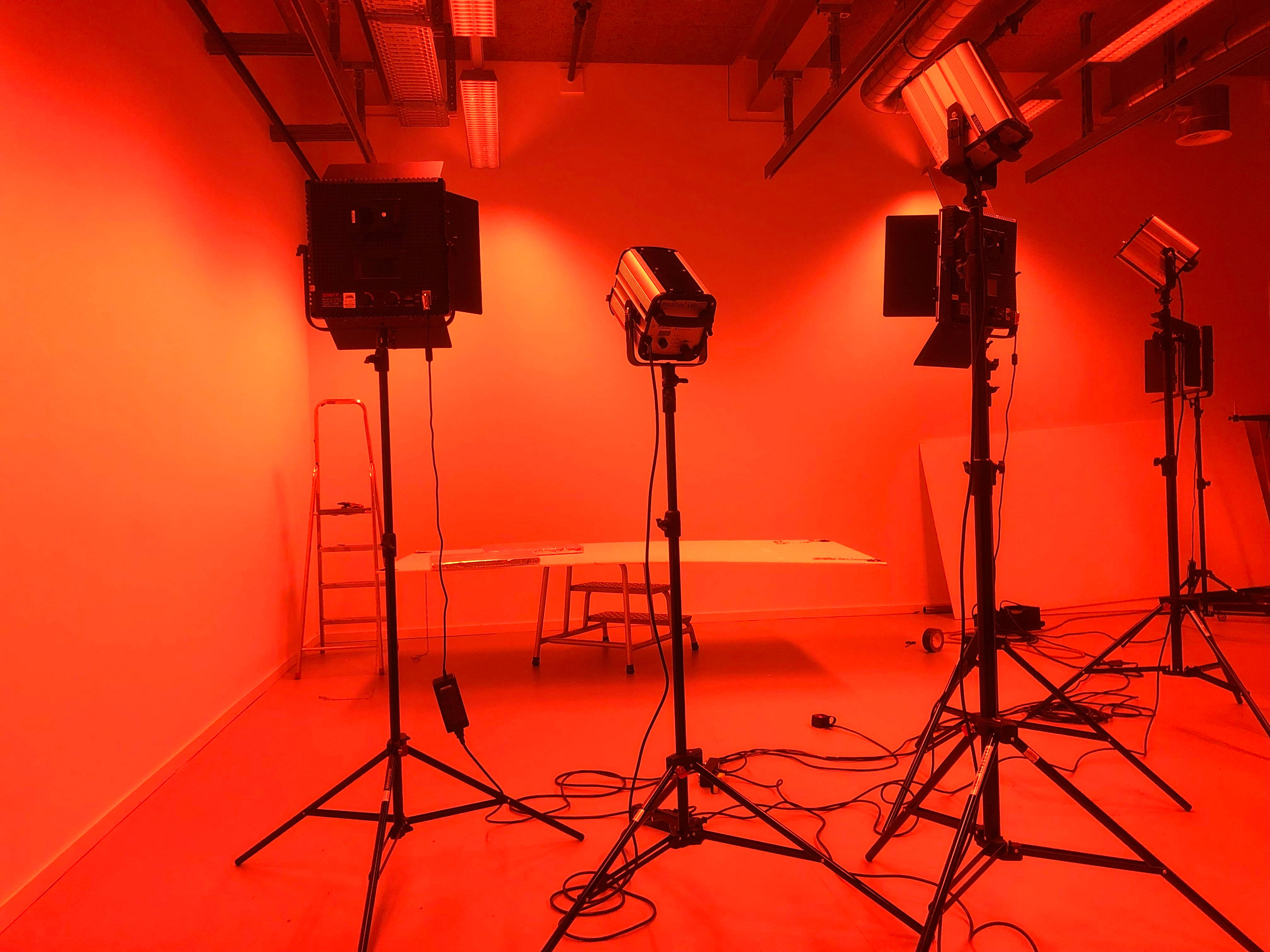 Studio 桌布 壁紙 — 一個被強烈紅光籠罩的攝影棚，有多支專業燈光放在燈架上，還有一把梯子靠著素牆。