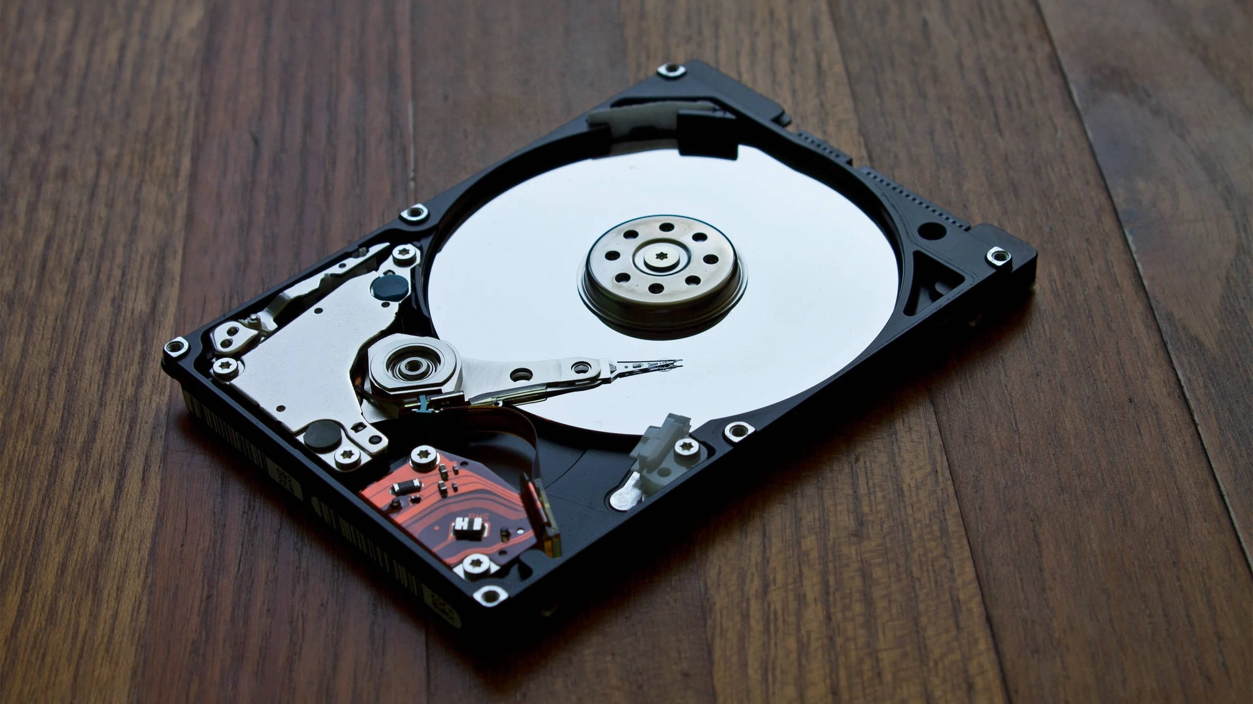 Hard Drive 桌布 壁紙 — 一個被拆解的硬碟驅動器在深色木質表面上顯露其內部組件。