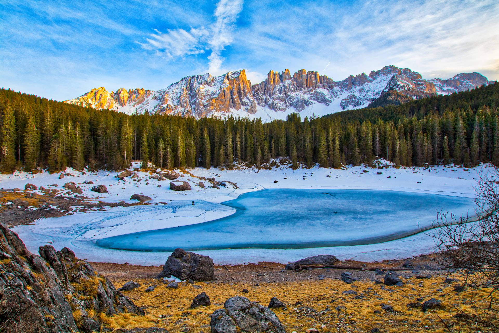 Mountain Landscape 桌布 壁紙 — 一個被白雪覆蓋的山谷中的冰凍湖泊，金色的陽光照亮了崎嶇的山峰和常綠森林。