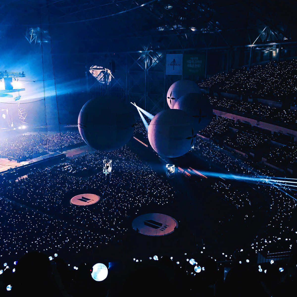 Bts Army Bomb 桌布 壁紙 — 一個被藍光籠罩的演唱會場地，漂浮著球體，以及人群中的一片發光手機燈海。