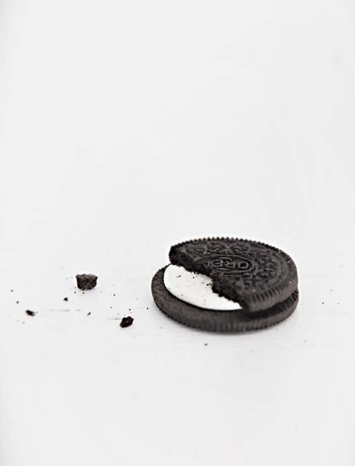 Minimalist Photography 桌布 壁紙 — 一個被部分食用的Oreo餅乾，碎屑散落在純白表面上。