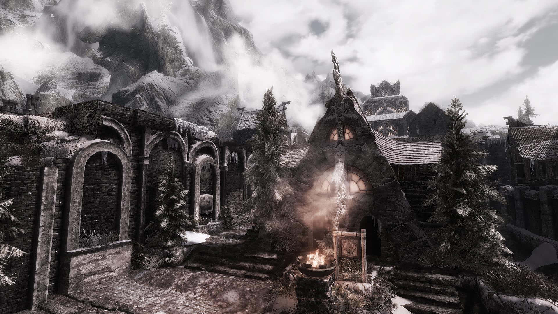 Skyrim Windhelm 桌布 壁紙 — 一個被雪覆蓋的中世紀村莊，坐落在霧氣繚繞的山脈中，擁有石頭建築和發光的壁爐。