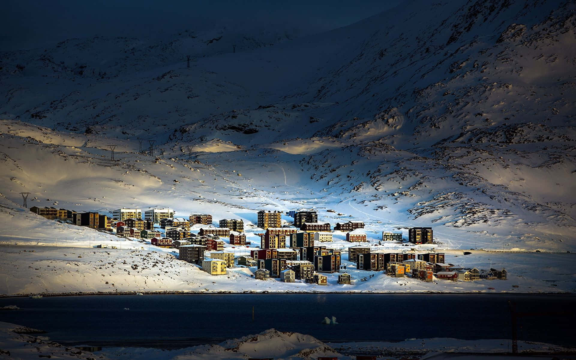 Greenland 桌布 壁紙 — 一個被雪覆蓋的山村，坐落在黑暗的湖泊旁，沐浴在戲劇性的暮光之中。