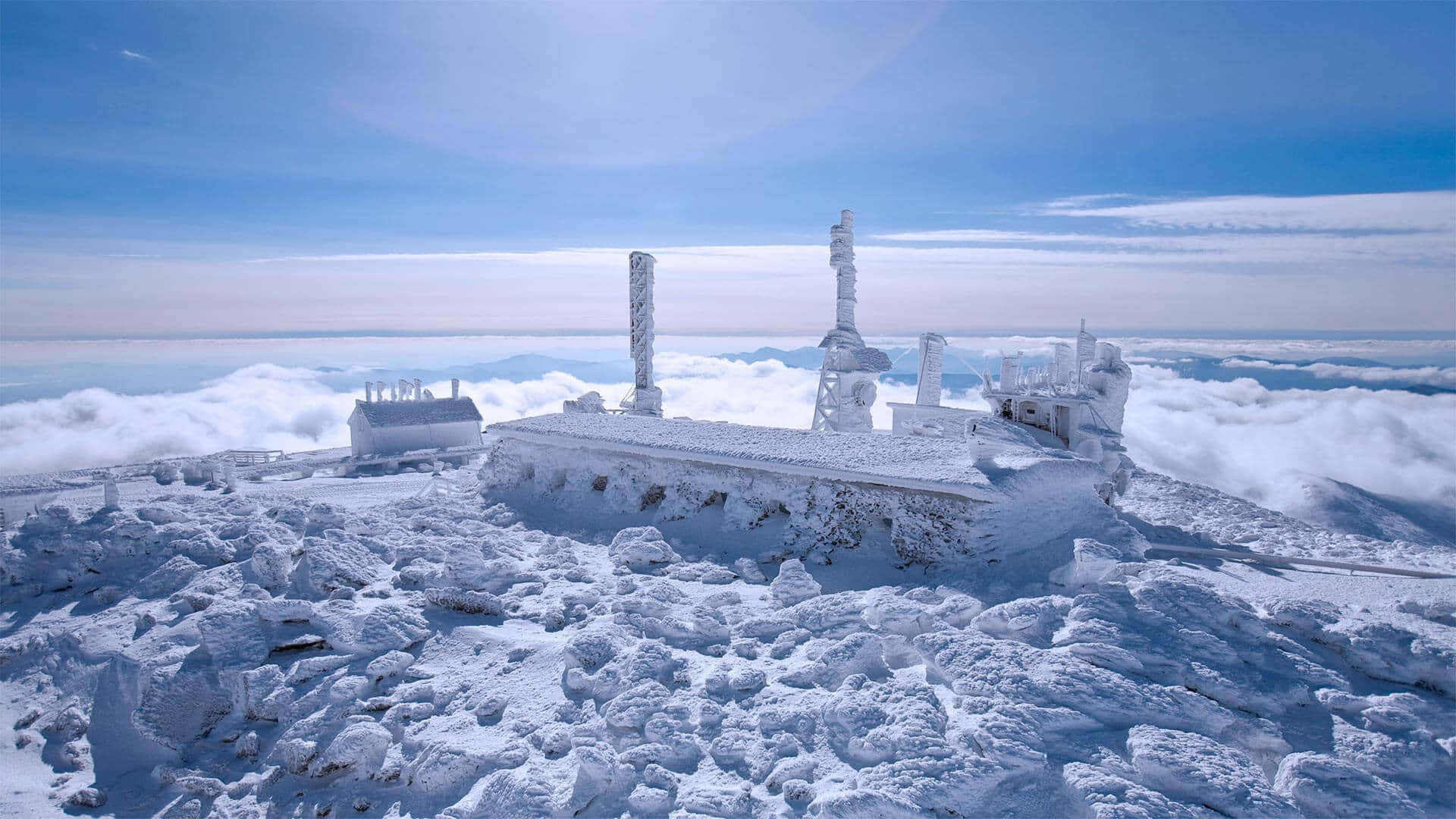 冬天 桌布 壁紙 — 一個被雪覆蓋的山間車站，坐落在雲海之上，天空清澈湛藍。