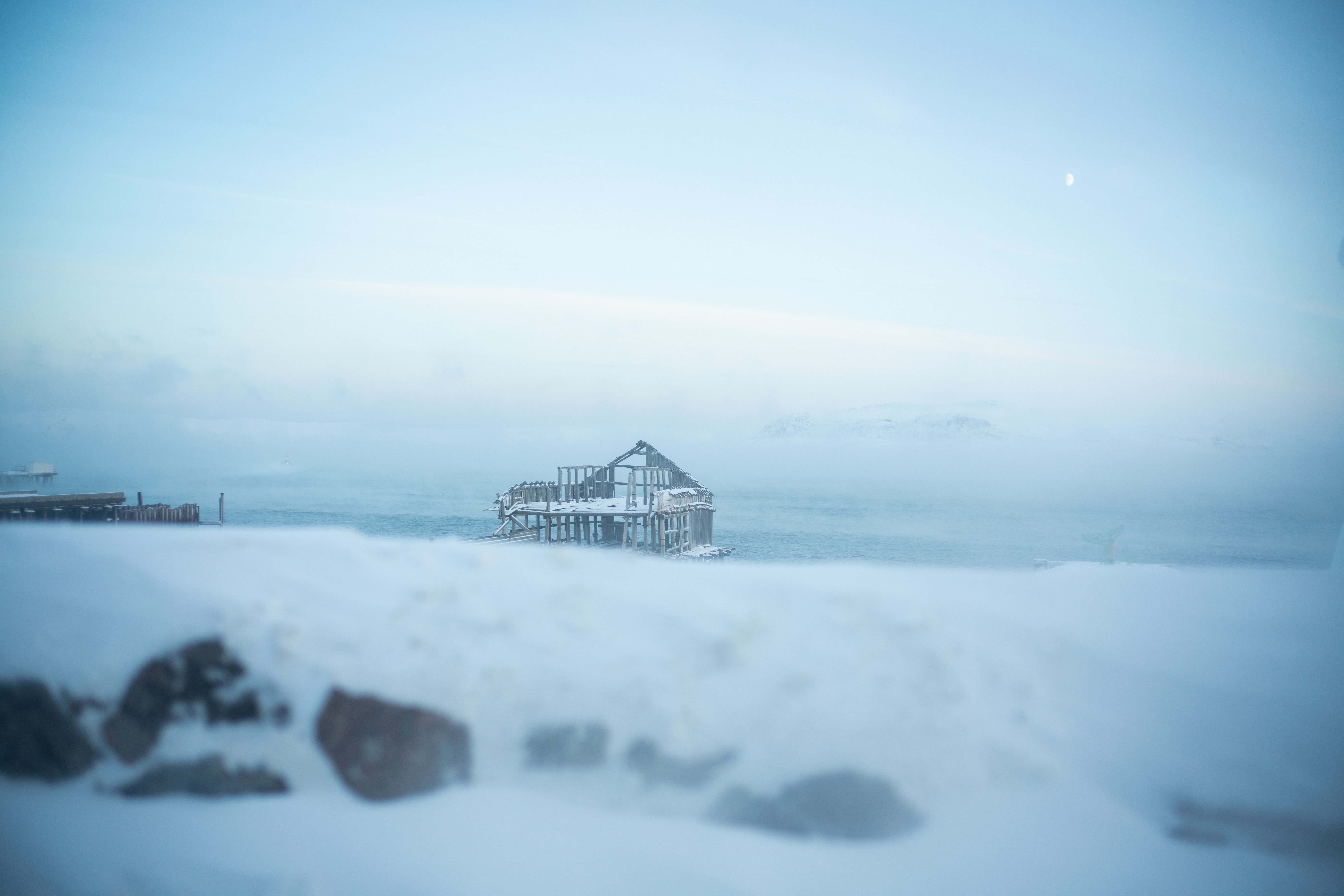 Winter 桌布 壁紙 — 一個被雪覆蓋的碼頭結構在霧濛濛的冬日大海中，在淡藍色的天空下被遺棄，可見月亮。