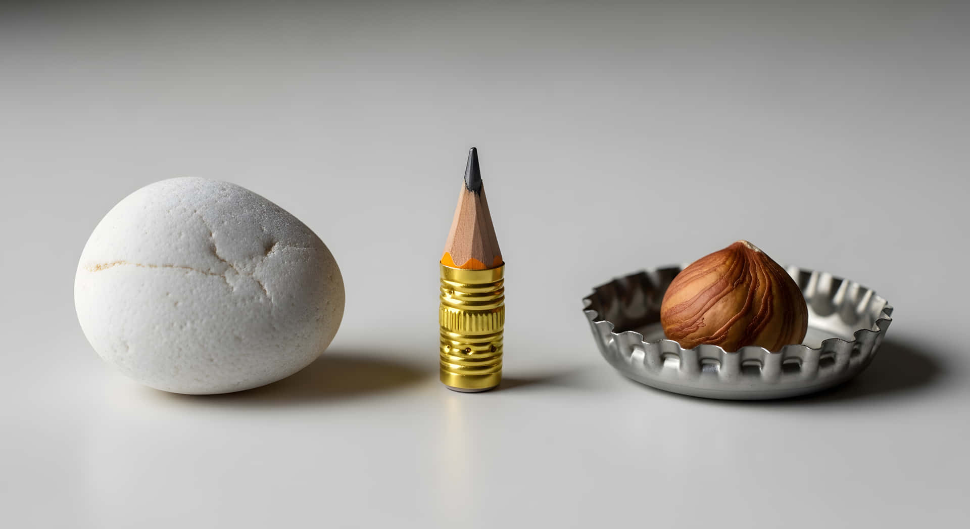 Minimalist Food Art Raisin Corn Kernel Cornbread still life featuring textured organic ingredients 壁紙 — 一個裂開的白雞蛋、一支帶金色金屬箍的削尖鉛筆，以及一顆榛子放在銀色瓶蓋內，置於純白表面上。