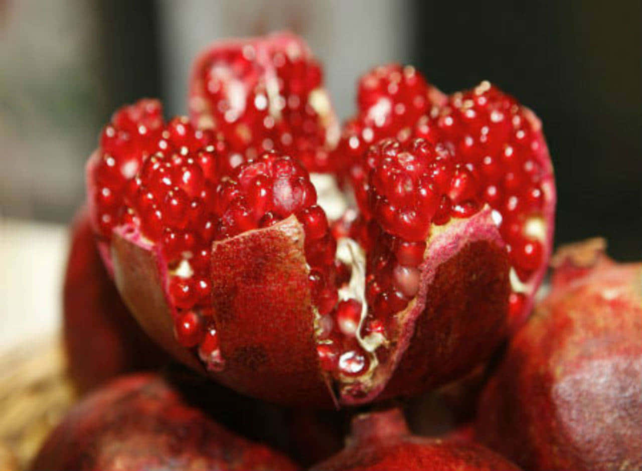 Red Fruit 桌布 壁紙 — 一個裂開的石榴特寫，在模糊的背景襯托下，露出閃閃發光的紅寶石色果粒。