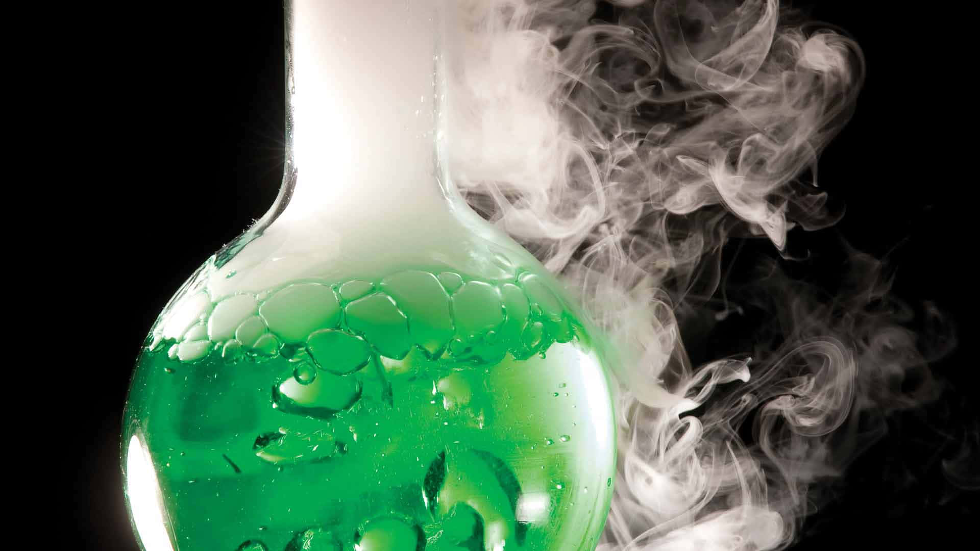 Green Chemistry 桌布 壁紙 — 一個裝滿冒泡綠色液體的玻璃燒瓶在黑色背景下釋放出旋轉的白煙。