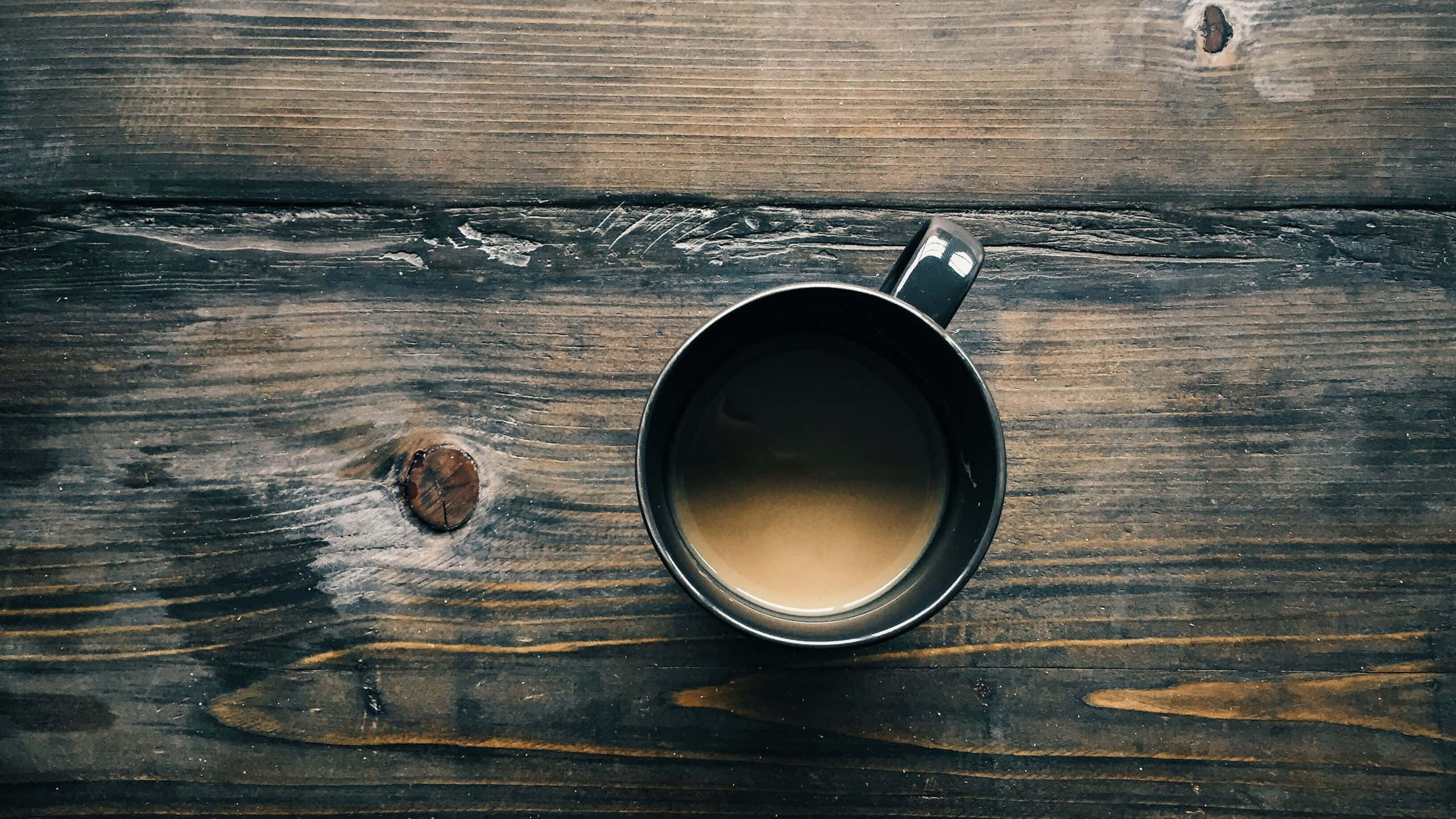 Coffee Aesthetic 桌布 壁紙 — 一個裝滿咖啡的黑色馬克杯放在一張深色質樸的木桌上，木紋和節疤清晰可見。