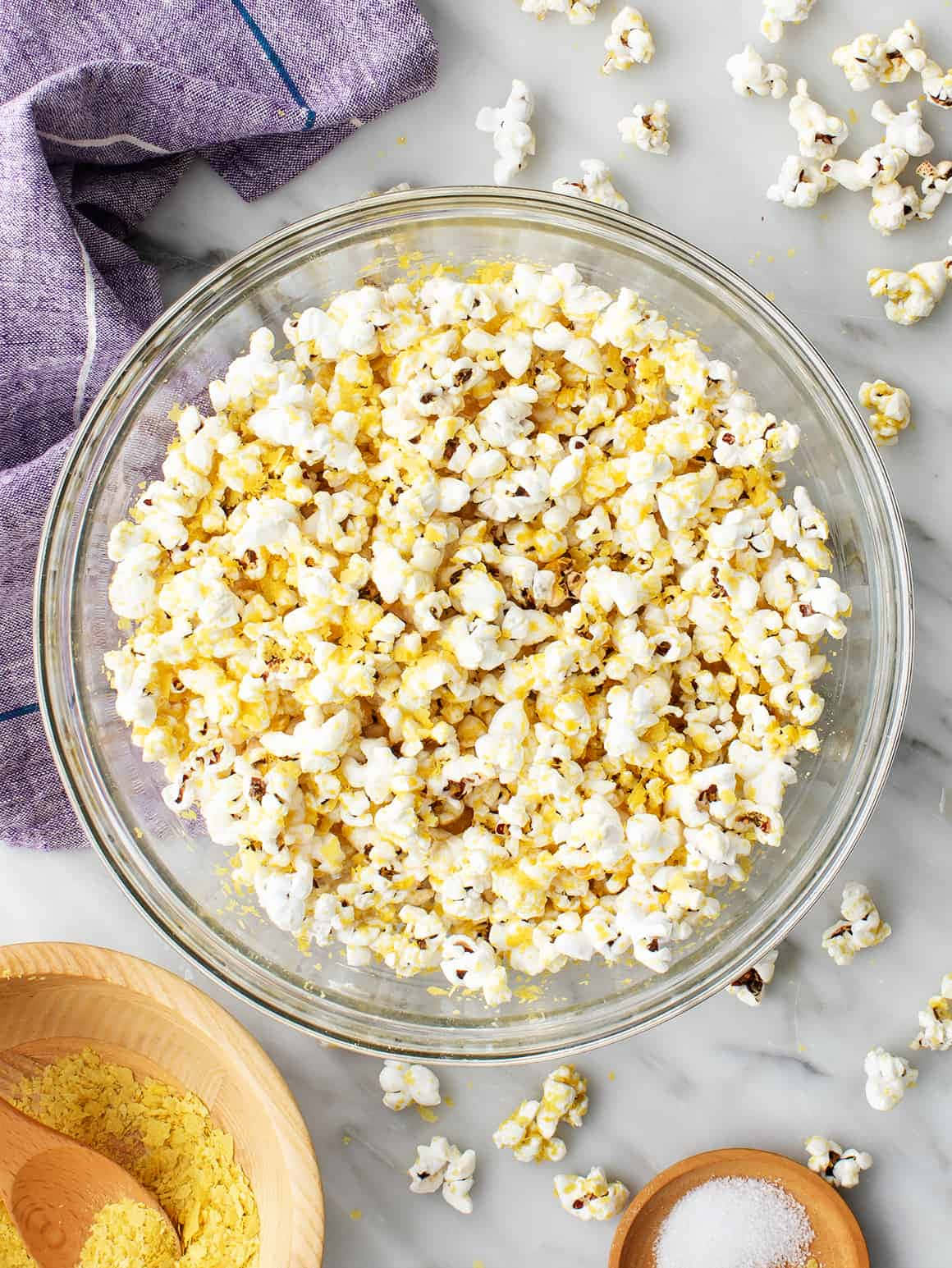 Popcorn 桌布 壁紙 — 一個裝滿奶油爆米花的玻璃碗放在大理石表面上，旁邊有木碗盛裝調味料和鹽。