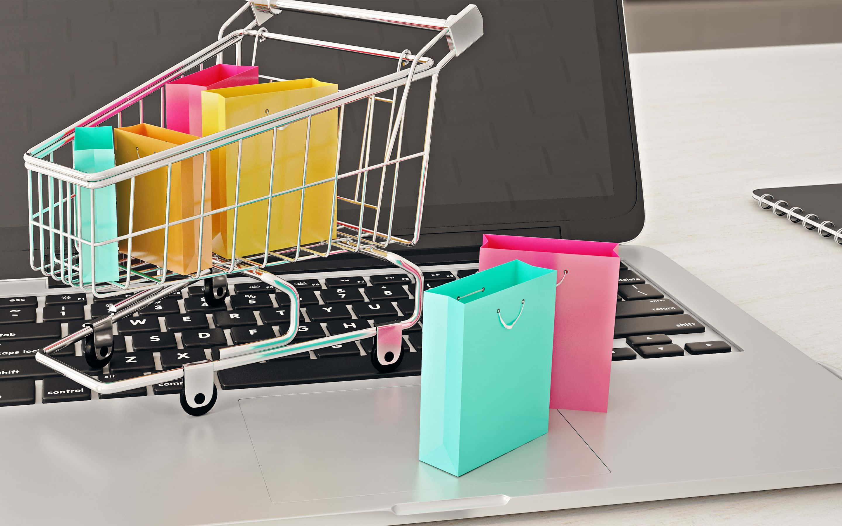 Shopping 桌布 壁紙 — 一個裝滿彩色袋子的微型購物車放在筆記型電腦鍵盤上，旁邊還有更多袋子。