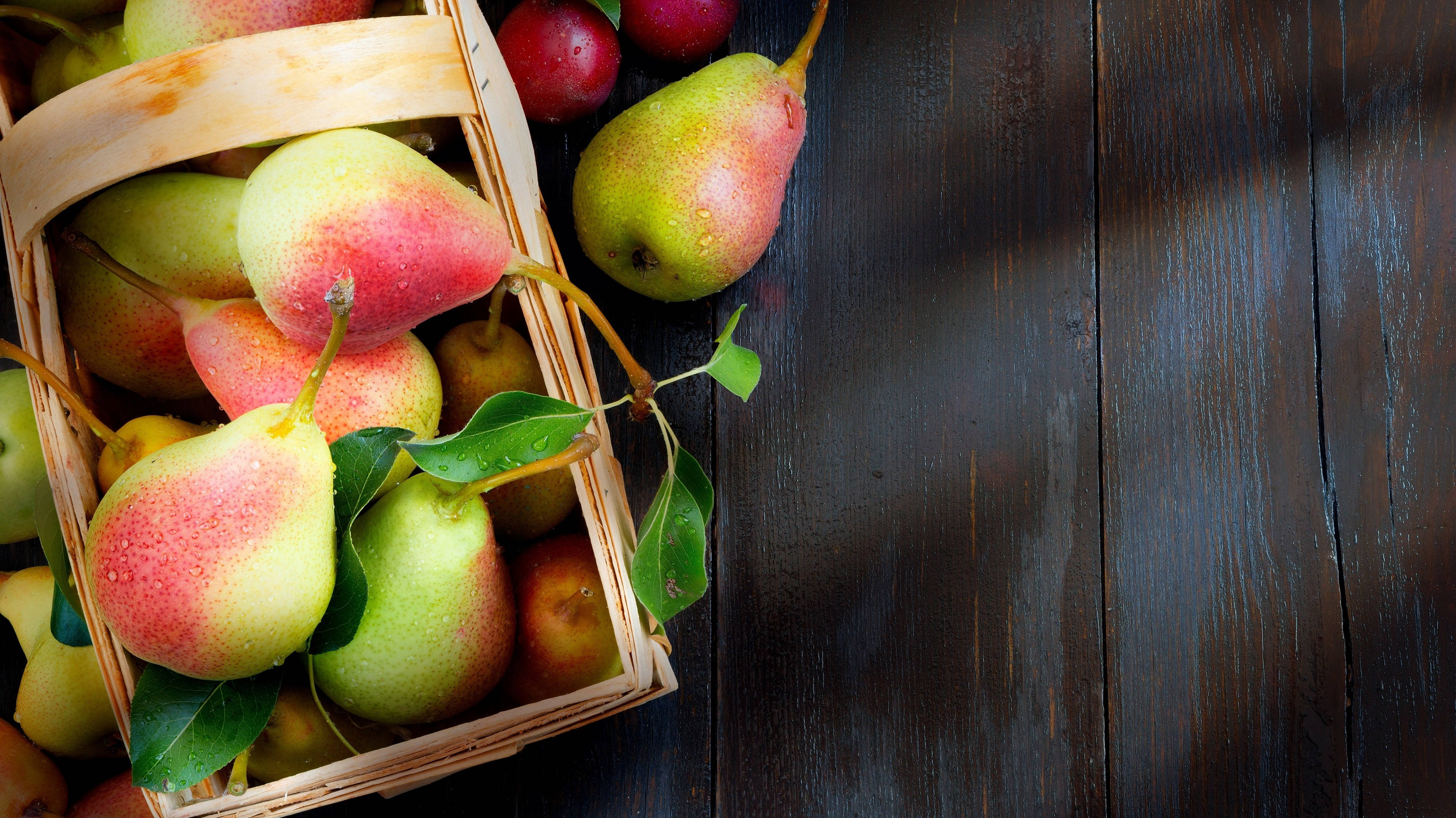 Fruits 桌布 壁紙 — 一個裝滿成熟梨子和紅蘋果的編織籃子放在深色木桌上，伴隨著新鮮的綠葉。