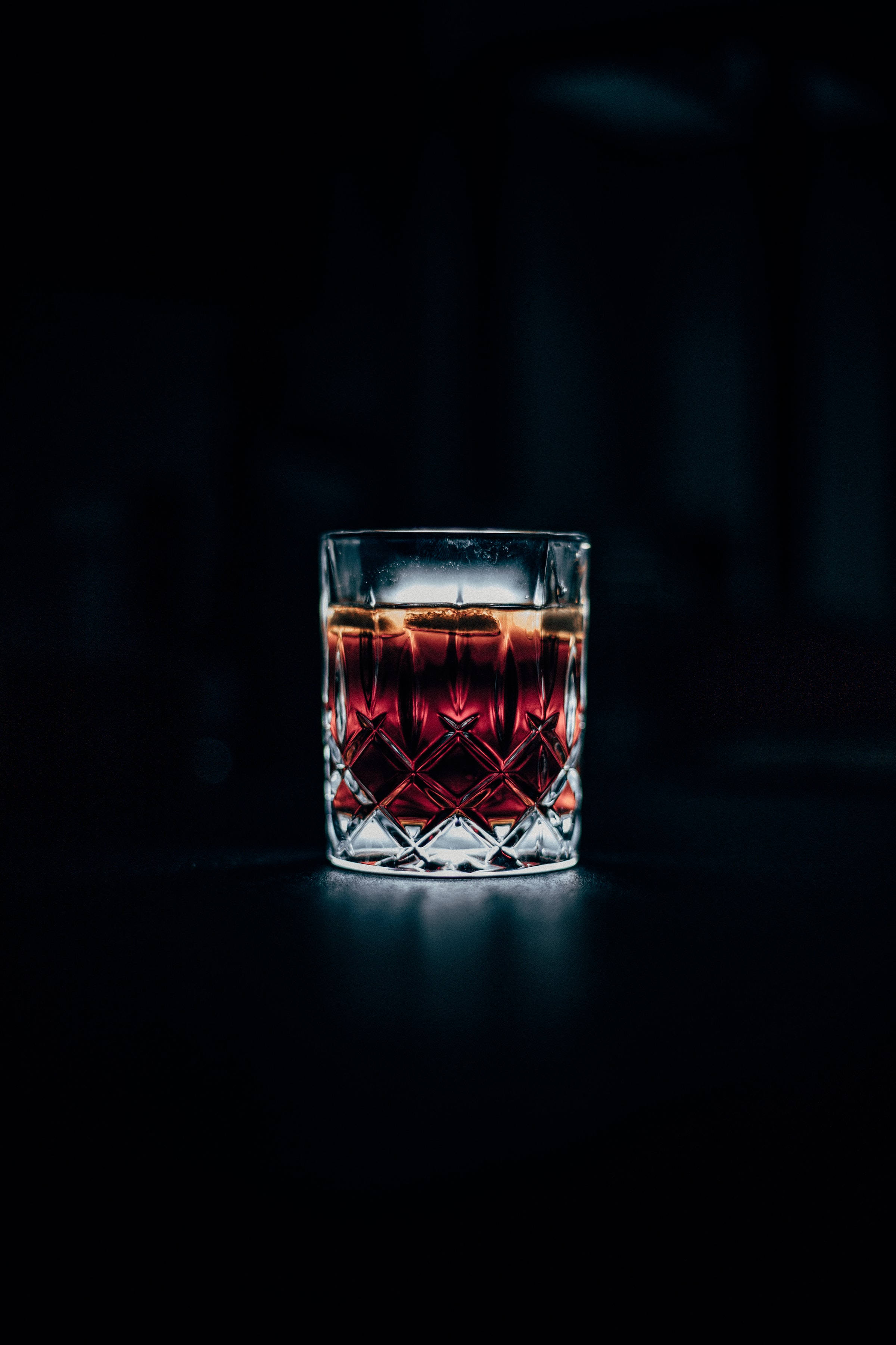 alcohol 桌布 壁紙 — 一個裝滿琥珀色液體和冰塊的水晶杯，在深黑色背景上溫暖地發光。