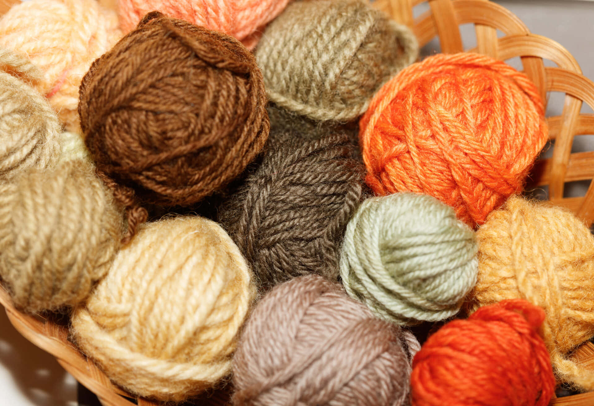 Knitting 桌布 壁紙 — 一個裝滿色彩繽紛毛線球的籃子，採用棕色、橙色和米色的大地色調。