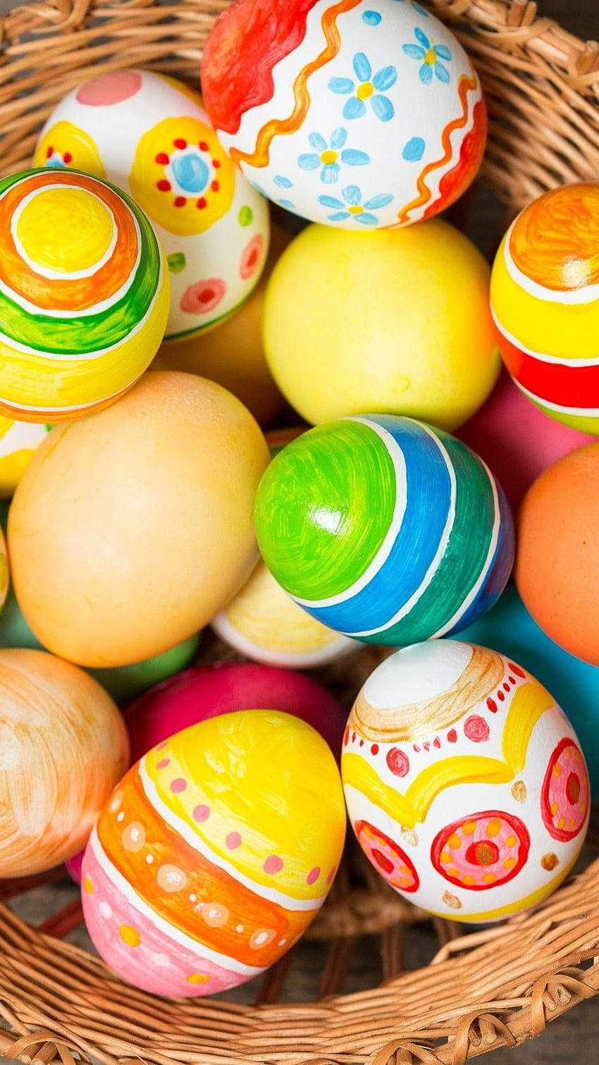 Easter Phone 桌布 壁紙 — 一個裝滿色彩鮮豔的復活節彩蛋的籃子，彩蛋上有花卉漩渦和粗條紋，顏色歡快。