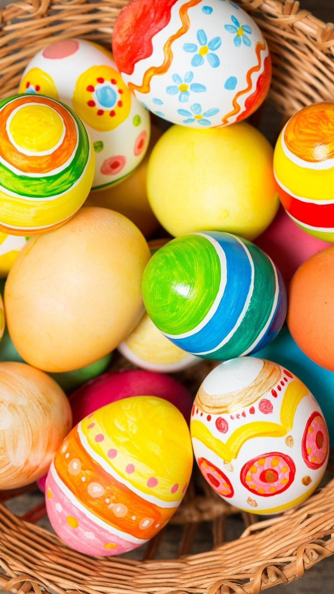 Easter iPhone 桌布 壁紙 — 一個裝滿色彩鮮豔的復活節彩蛋的籃子，彩蛋上繪有花卉漩渦和粗條紋，採用歡快的粉彩和原色。
