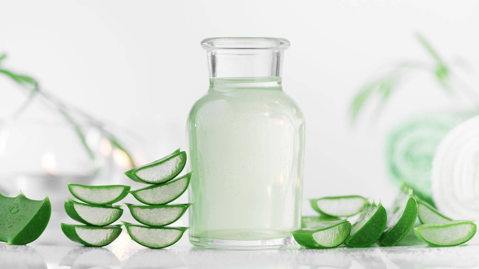 Plant 桌布 壁紙 — 一個裝滿蘆薈凝膠的透明玻璃瓶，周圍是新鮮的綠色蘆薈片，放在明亮的白色表面上。